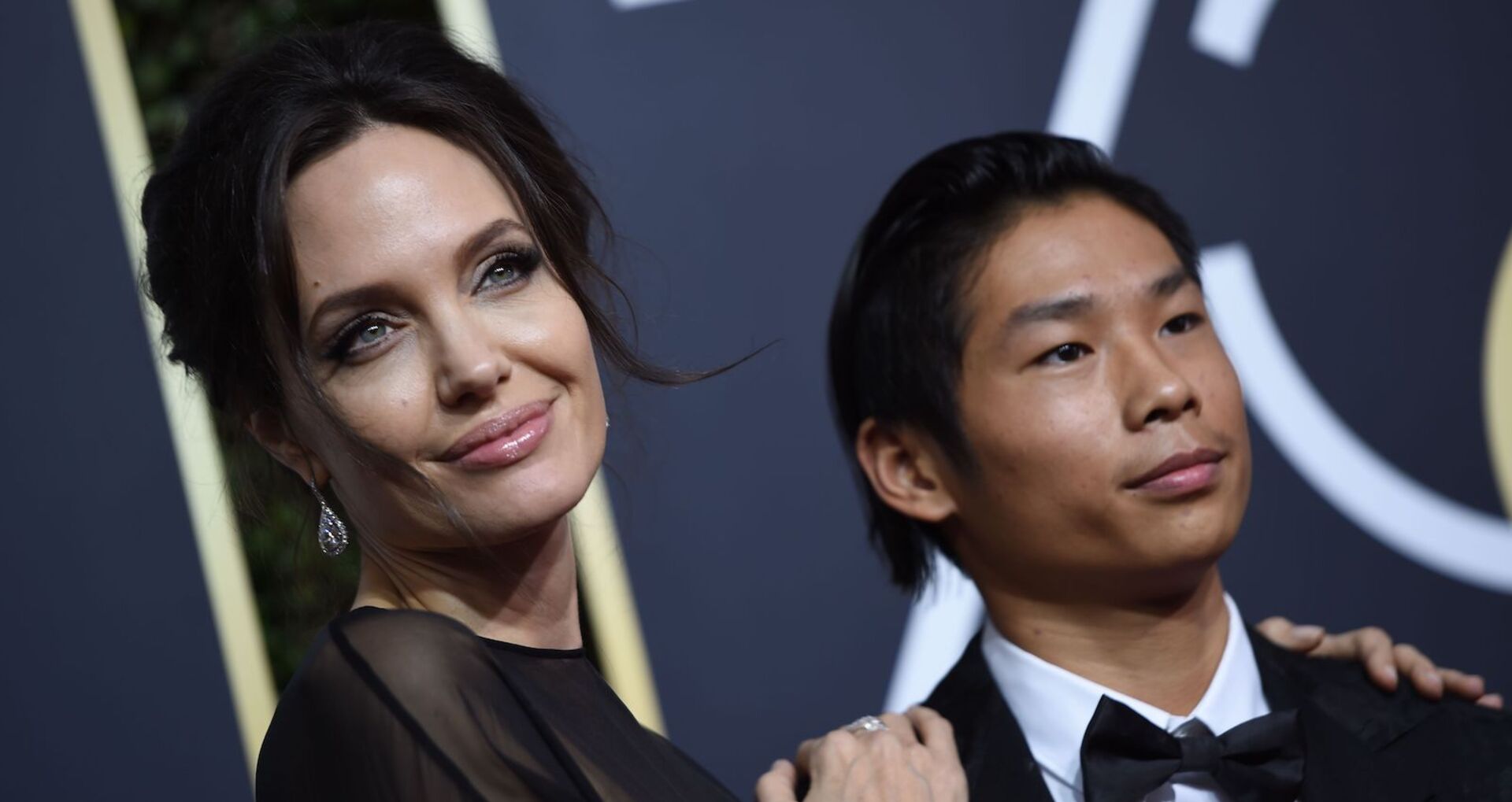Angelina Jolie trägt hochgesteckt dunkle Haare und ein schwarzes Kleid. Pax trägt einen schwarzen Smoking und ein weißes Hemd.