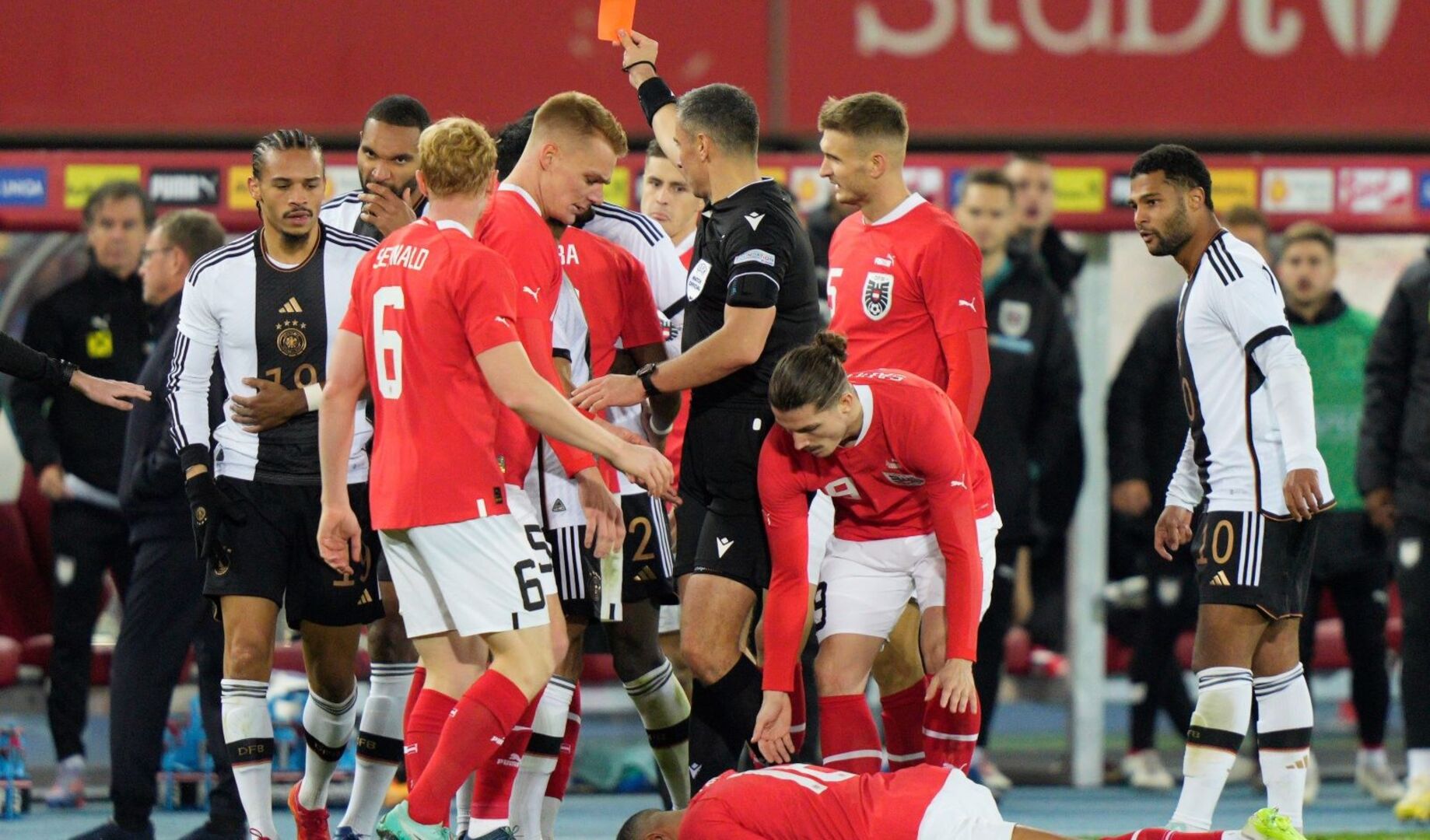 Gemenge deutscher und östererichischer Spieler, ein Österreich liegt am Boden. Der Schiedsrichter zeigt die rote Karte.