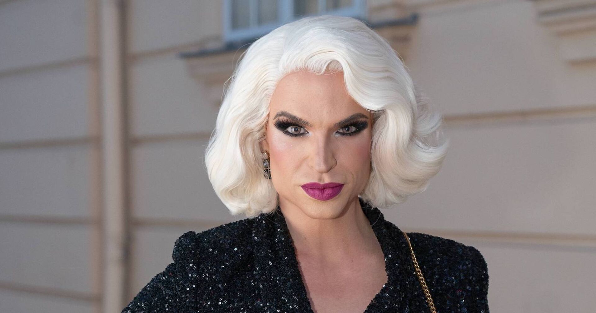 Tamara Mascara ist eine Dragqueen und trägt eine weiße Marilyn Monroe Perrücke und einen schwarzen Anzug mit Pailetten.