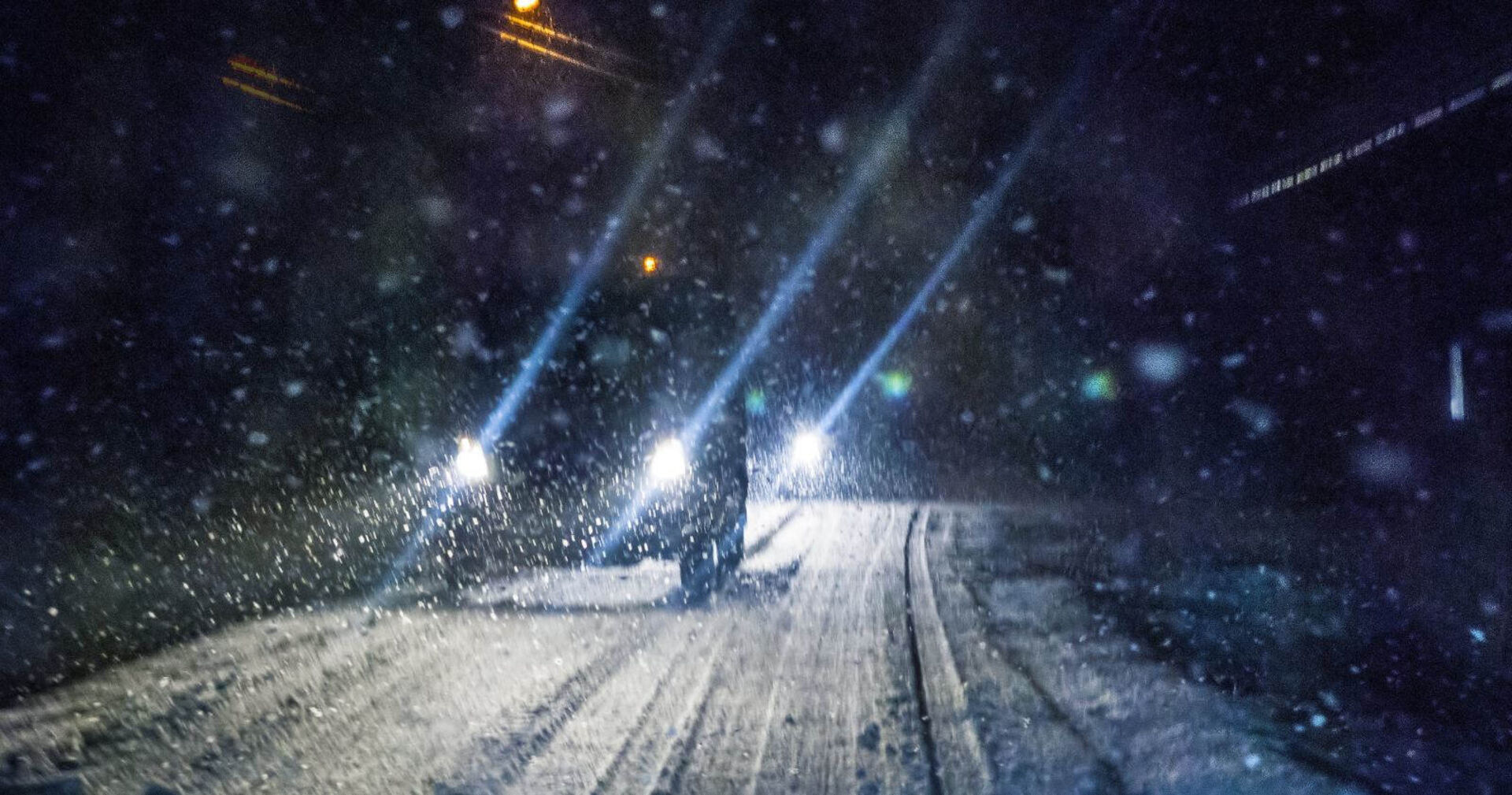 Ein Auto fährt nachts auf einer Schneefahrbahn.
