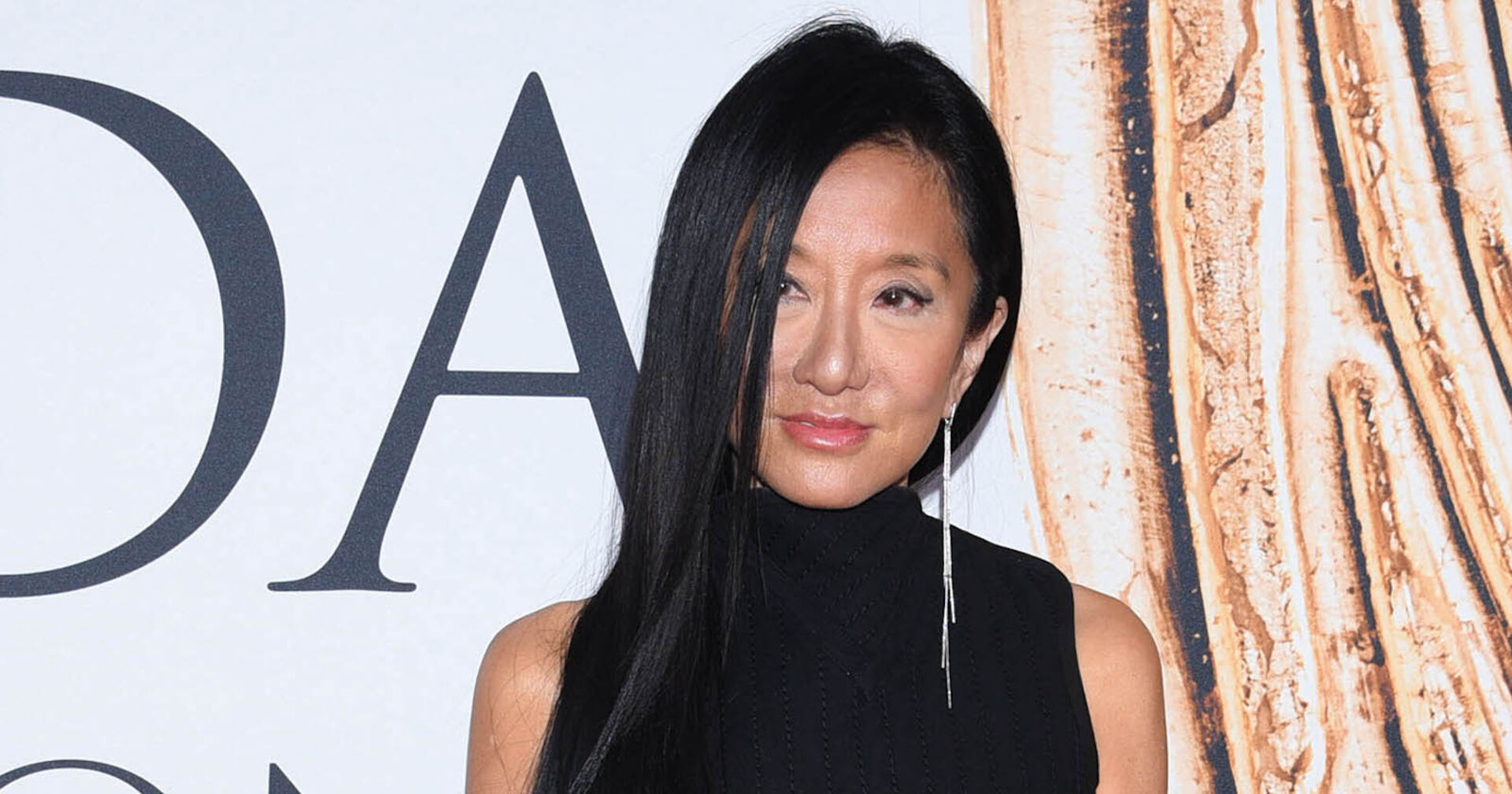 Vera Wang trägt offene braune Haare und steht vor einer weißen Fotoleinwand.