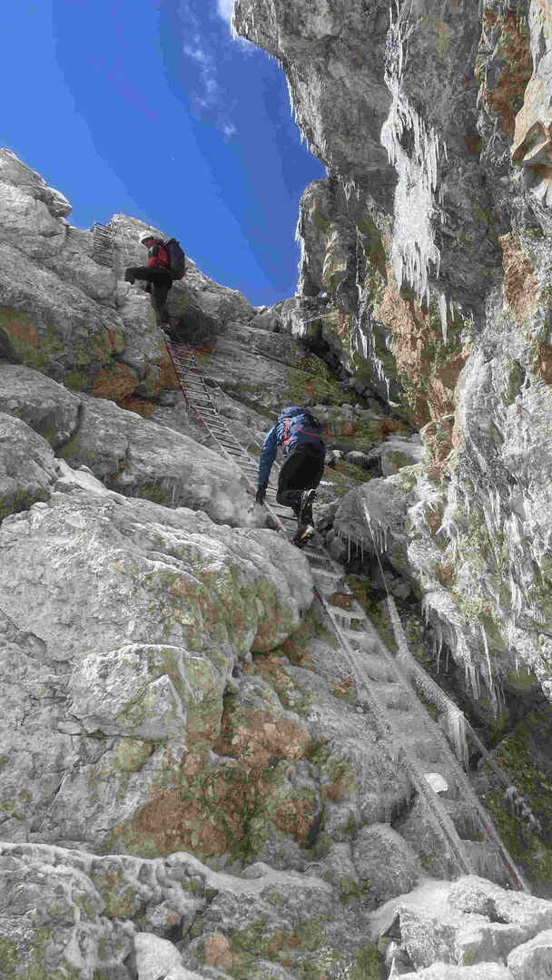 Zwei Bergsteiger auf einem vereisten Klettersteig mit Leiter.