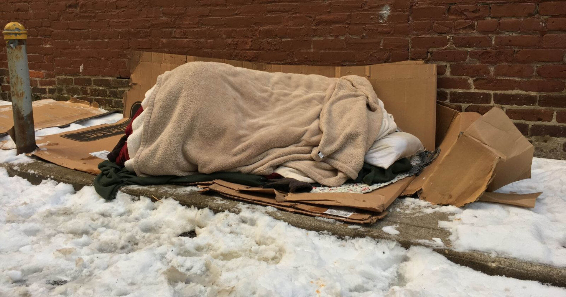 Ein Obdachloser schläft bei Schnee auf der Straße.