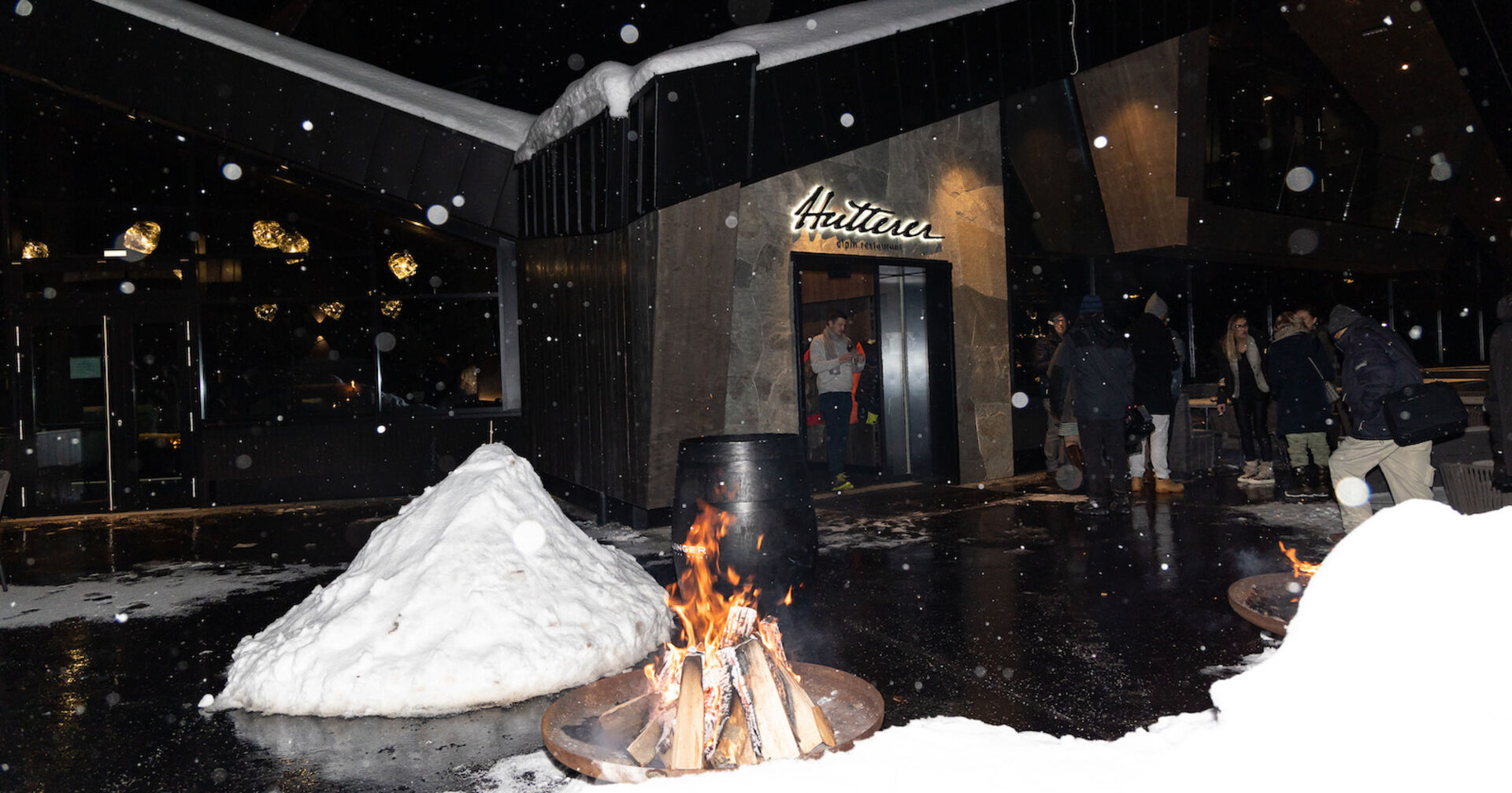 Nachtaufnahme vim Eingang mit Feuerschalen und viel Schnee