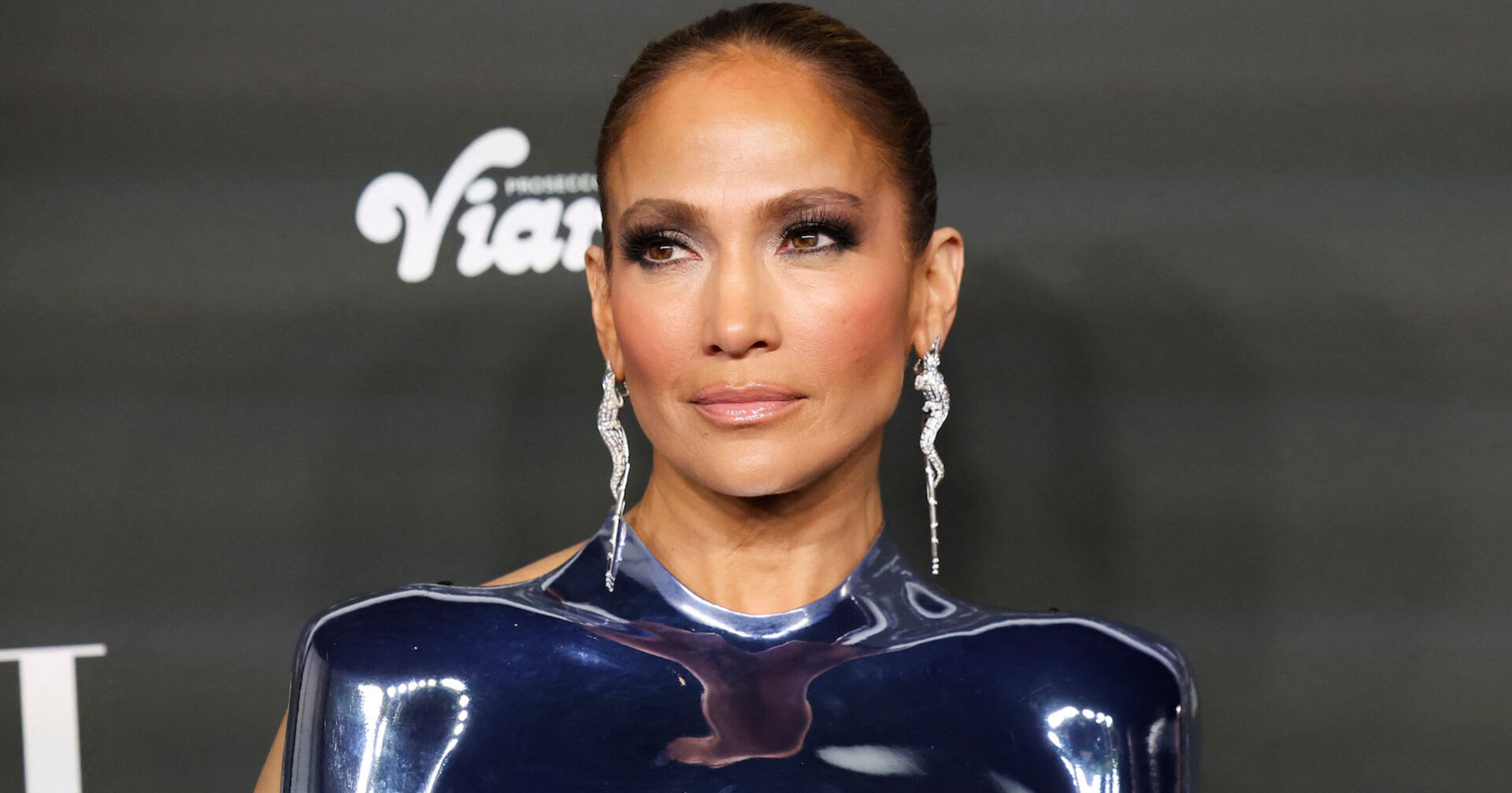 Jennifer Lopez mit strengen, gegelten Haaren und großen Diamantohrringen. Dazu ein metallenes Oberteil.