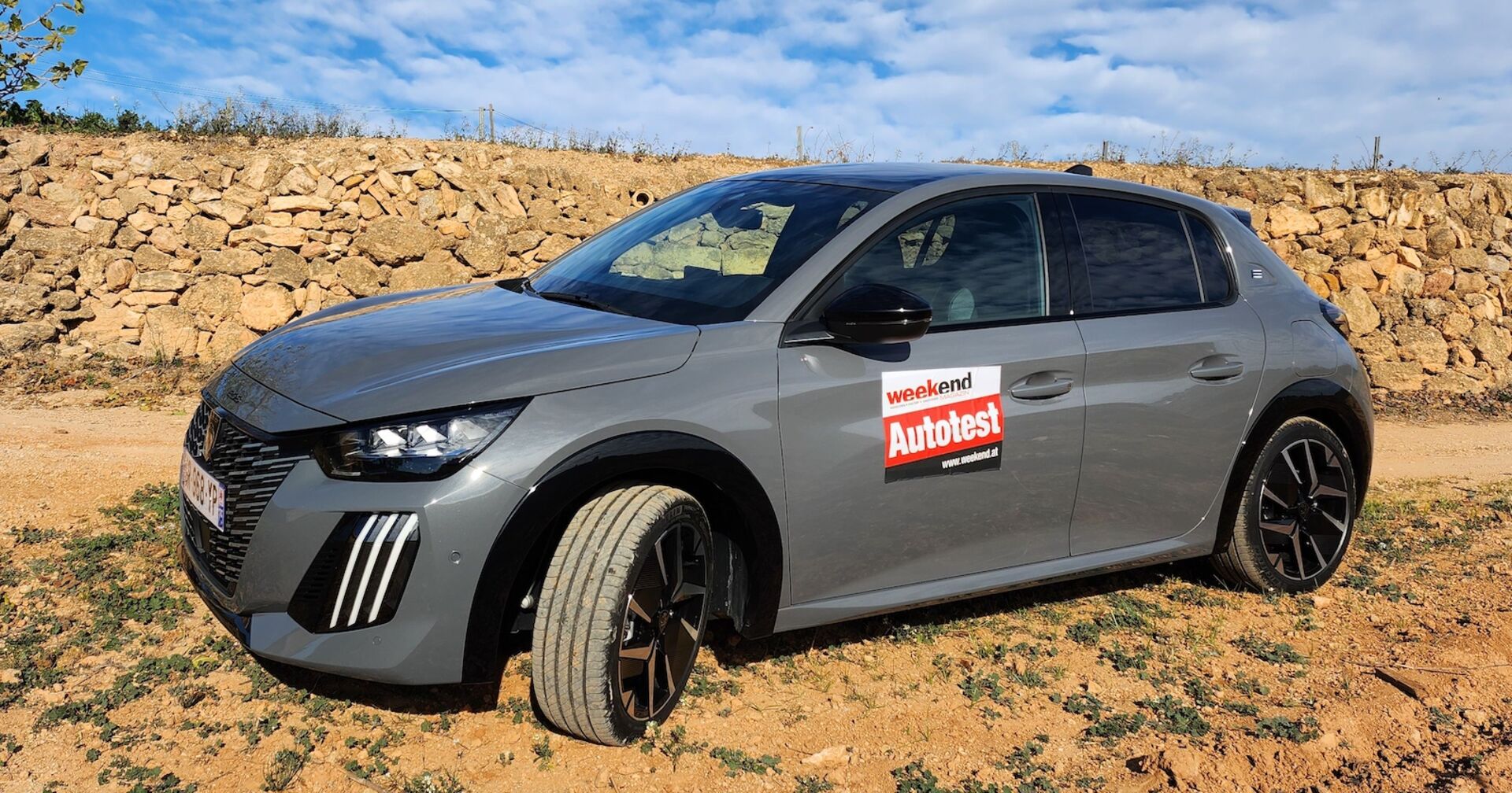 Der Peugeot E 208 vor einer Steinmauer