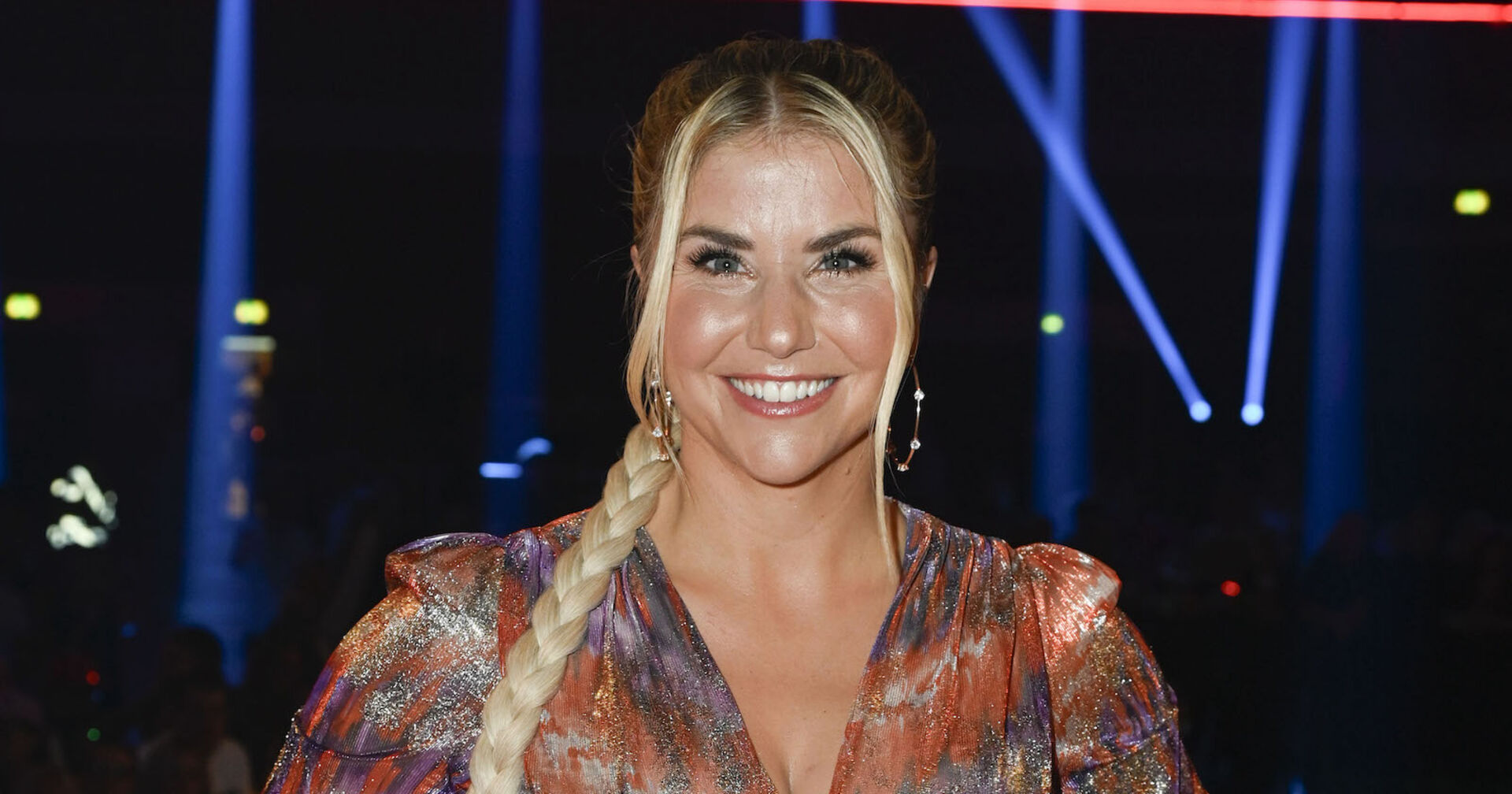 Beatrice Egli mit einem langen blonden Zopf und einer bunten Bluse.