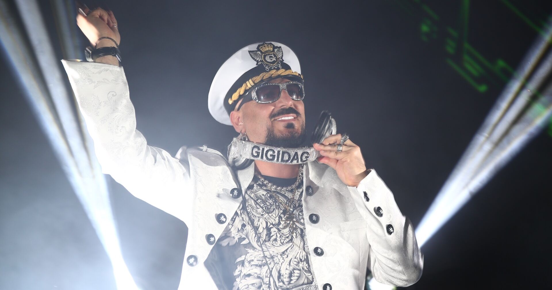 Gigi D'Agostino mit einer weißen Jacke und einem Kapitän-Hut bei einem DJ-Set.