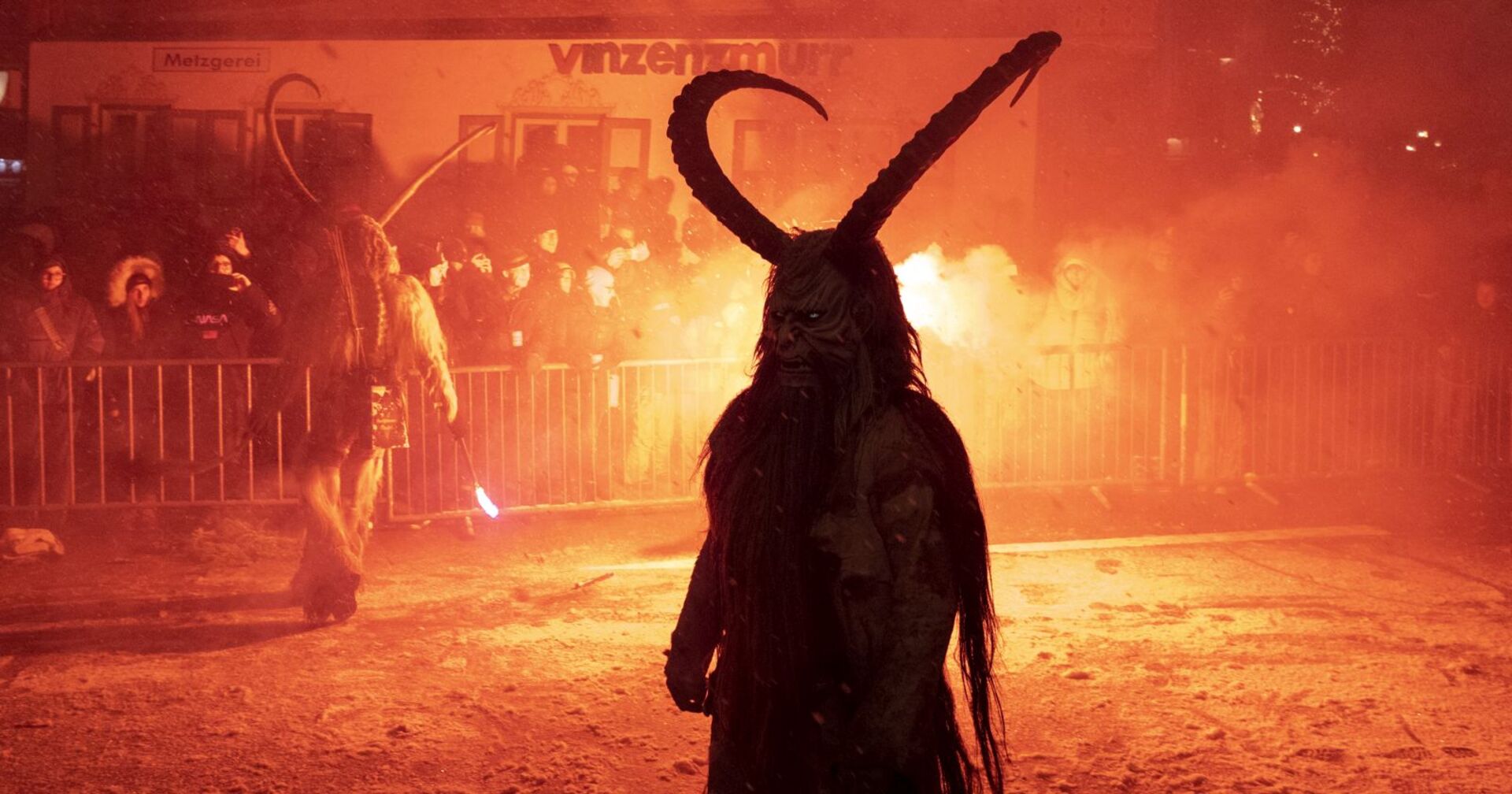 Ein Krampus steht vor dem Publikum, hinter ihm Feuer.