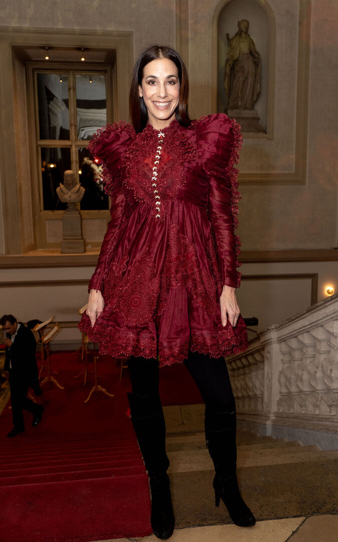 Nina Hartmann mit einem imposanten roten Kleid und schwarzen Stiefel an einer Treppe im Palais Auersberg.