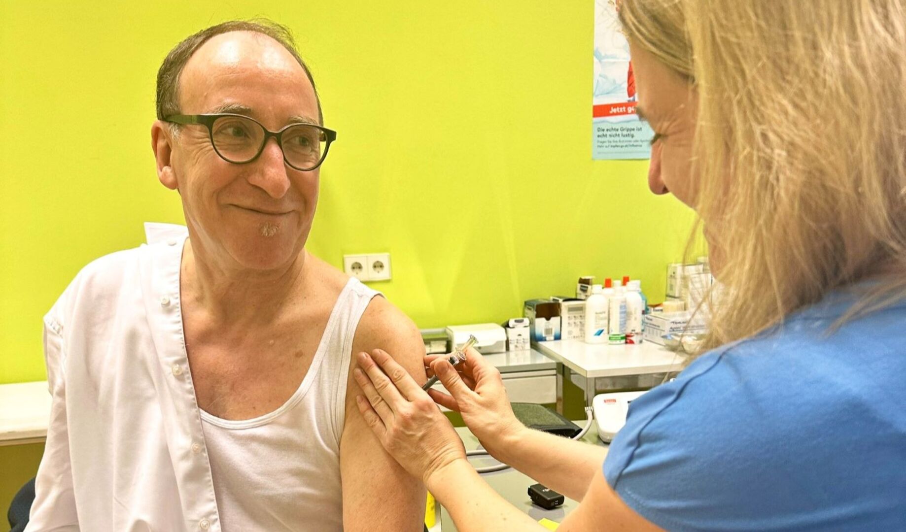 Rauch im Unterhemd, eine Ärztin setzt eine Spritze an seinem Arm an.