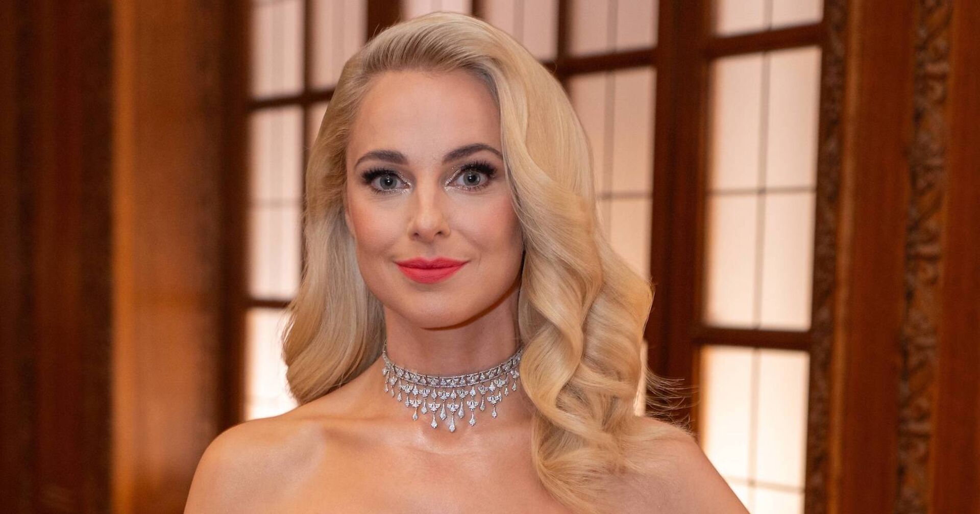 Silvia Schneider hat offene blonde, gewellte Haare und ein Abend-Make-Up. Dazu trägt sie eine Kette aus Diamanten.