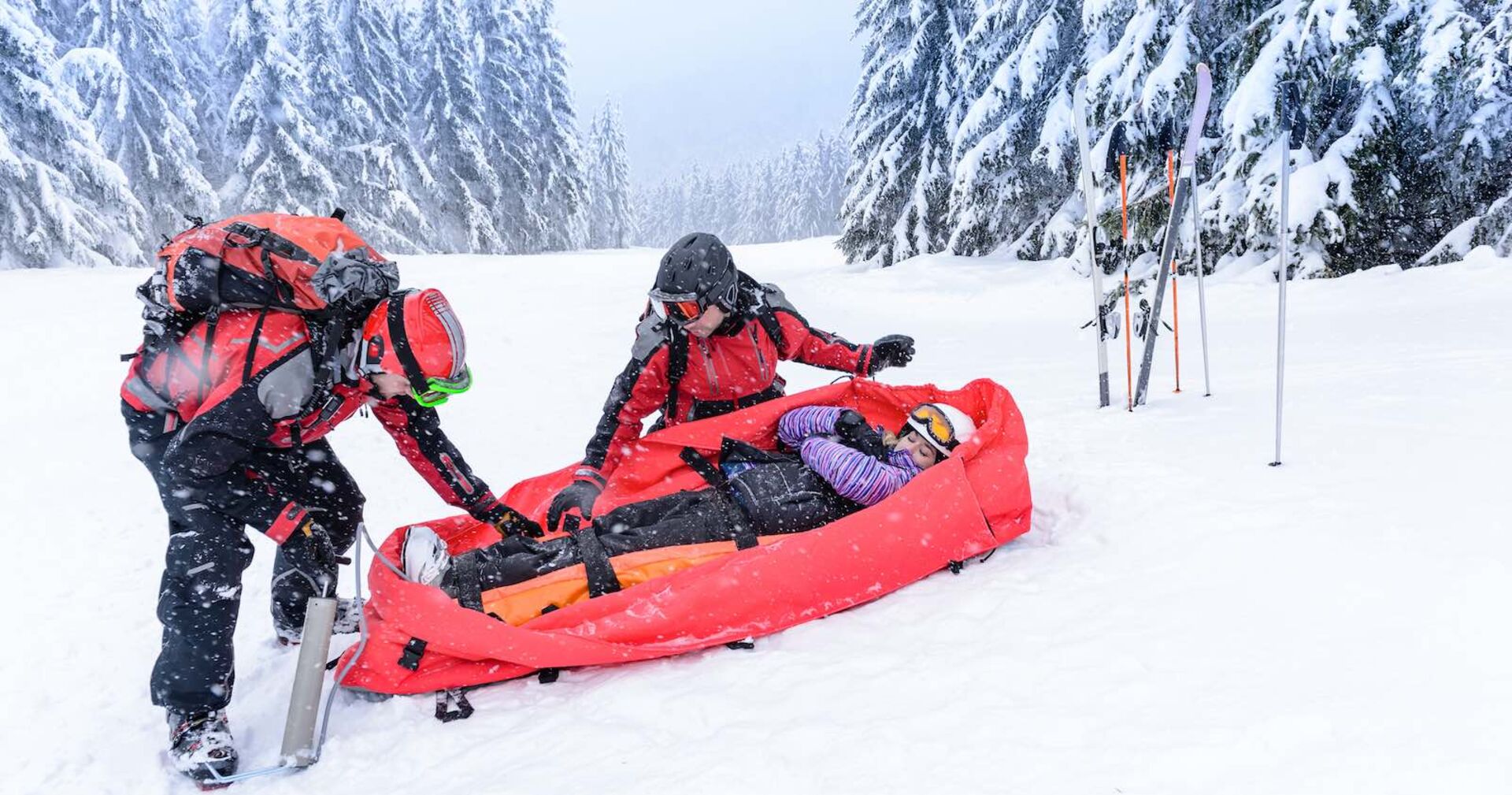 Zwei Rettungskräfte bergen einen verletzte Person auf der Piste.