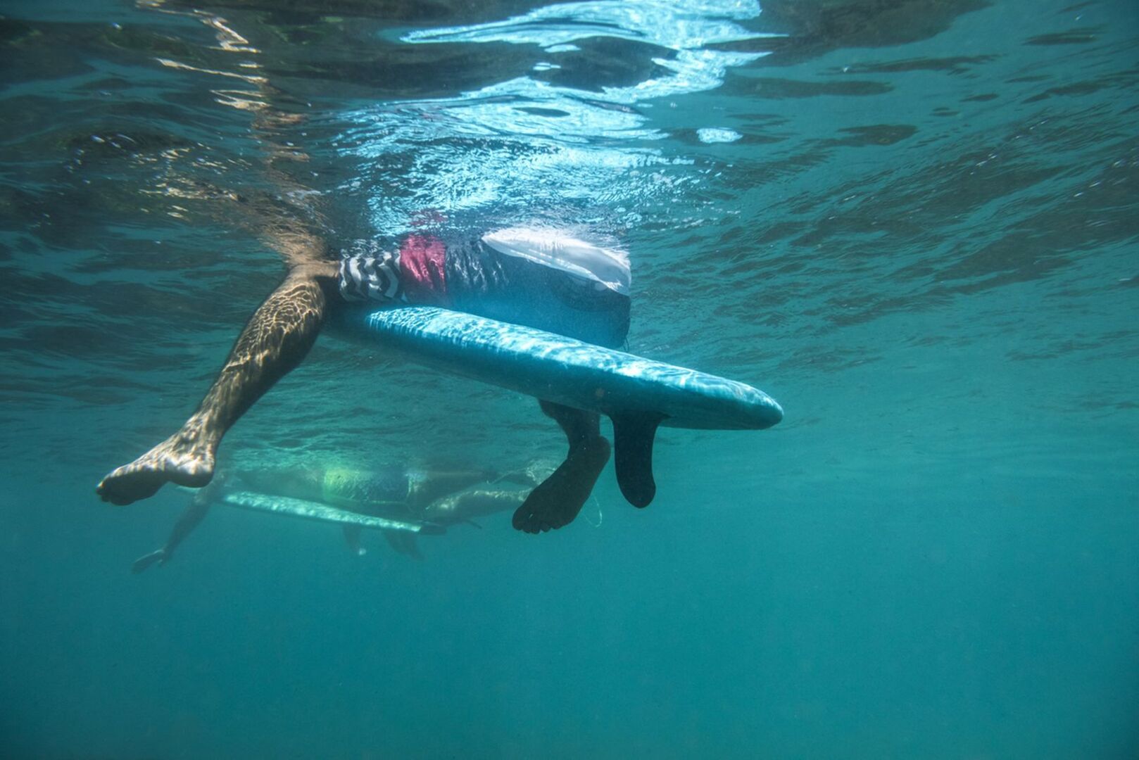 Die Beine eines Surfers unter Wasser.