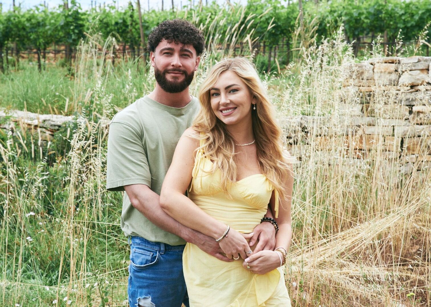 Umut umarmt Jana-Maria und trägt ein grünes Top und eine Jeans. Sie trägt offene blonde Haare und ein gelbes Kleid.