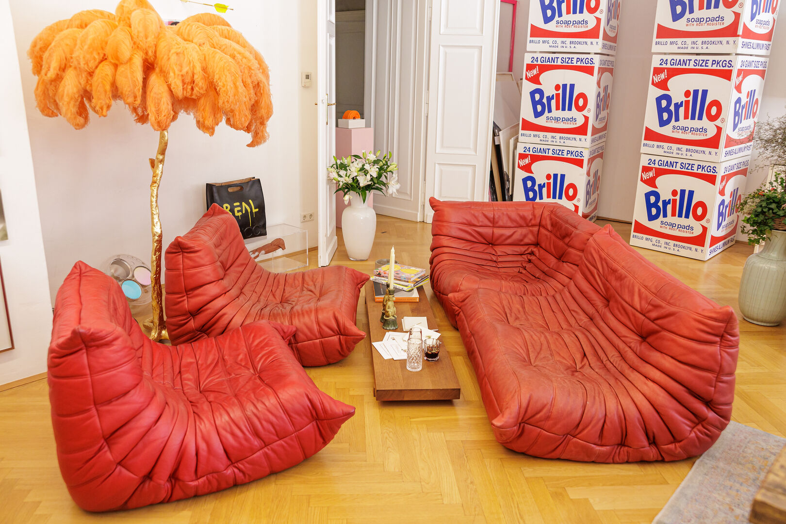 Ein Wohnzimmer mit rotem Ledersofa, Palmenlampe und Brillo-Boxen