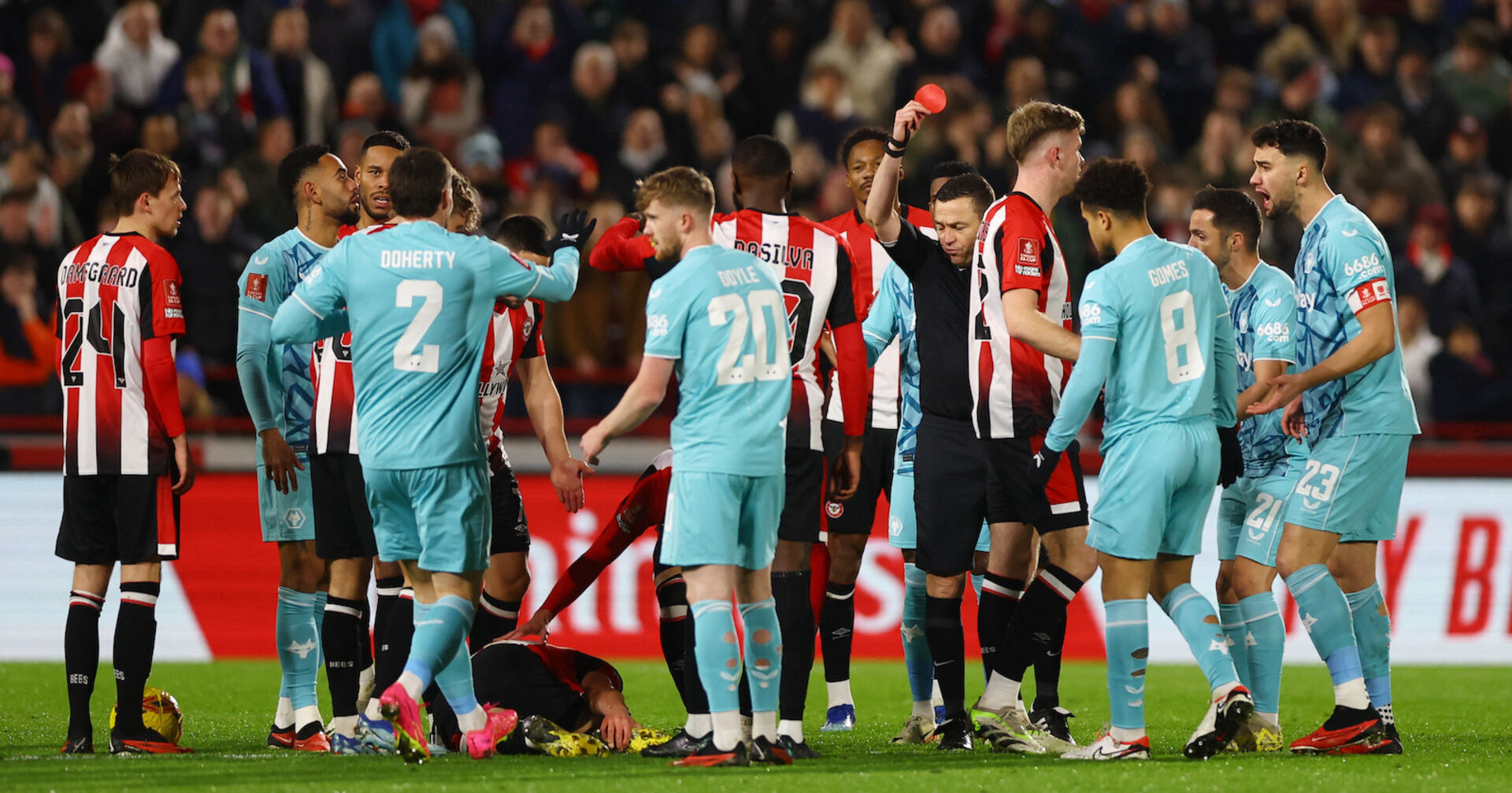 Mehrere Fussballspieler versammeln sich um den Schiedsrichter, der eine rote Karte hoch hält