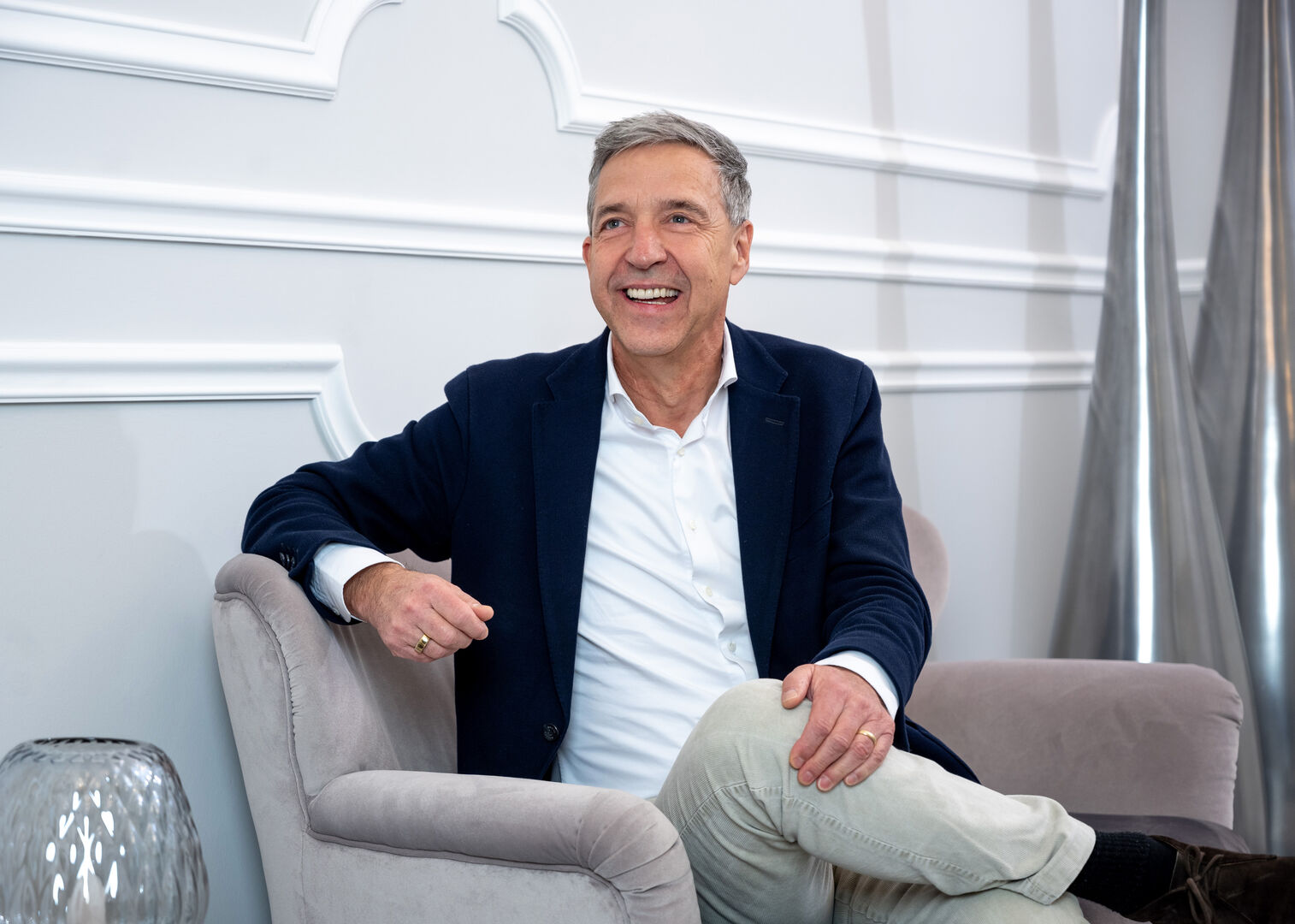 Gerhard Mosser, der auf einer beigen Couch sitzt und in die Kamera lächelt