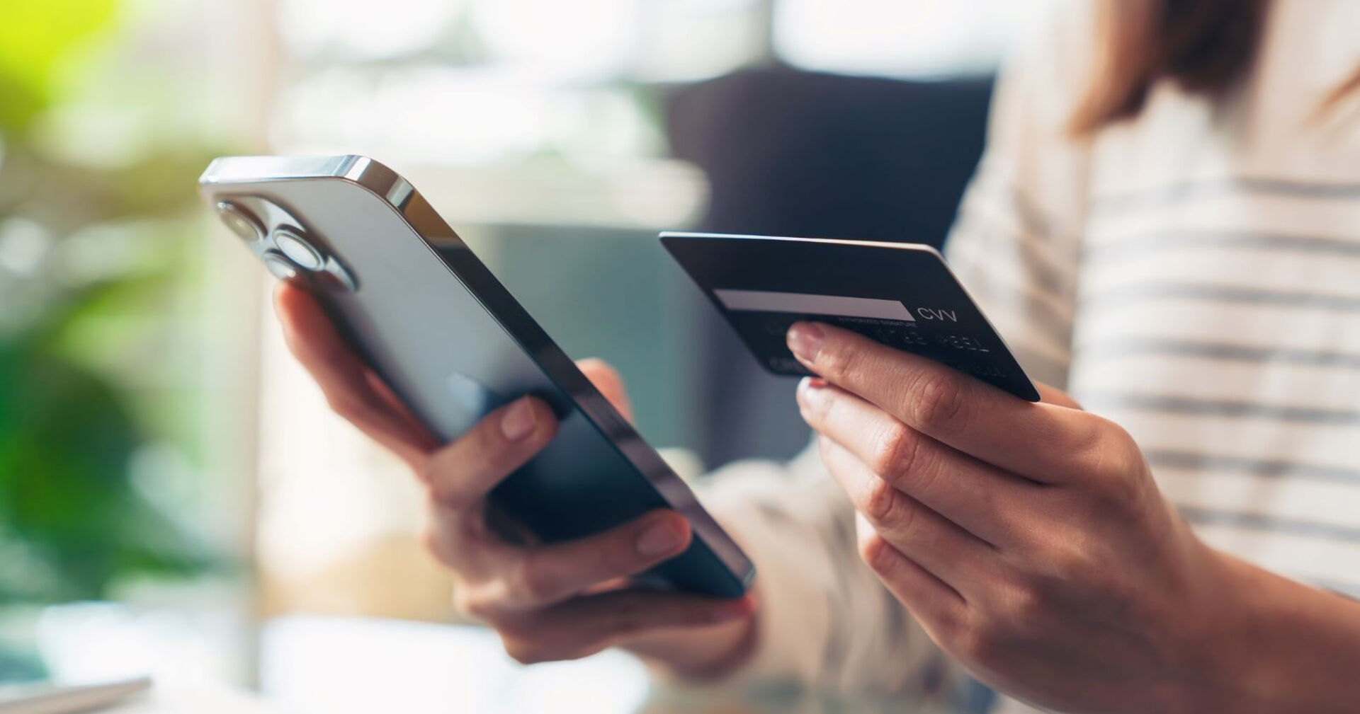 Eine Frau hält in einer Hand ein Smartphone und in der anderen eine Bankkarte.
