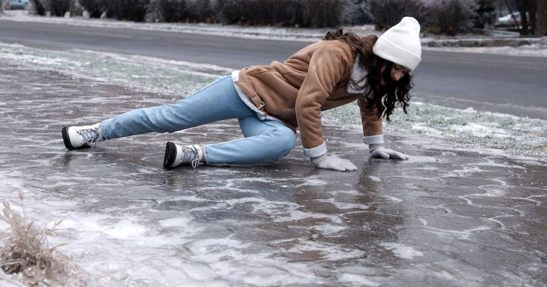 Eine Frau ist auf einer rutschigen Fläche ausgerutscht und gestürzt. Gehweg und Straße sind völlig vereist