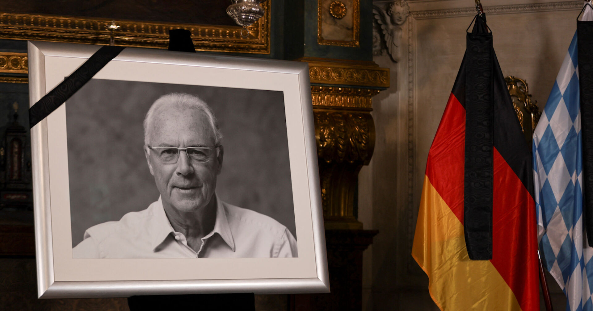 Ein Schwarzweißfoto des verstorbenen Franz Beckenbauer neben einer Deutschlandfahne.