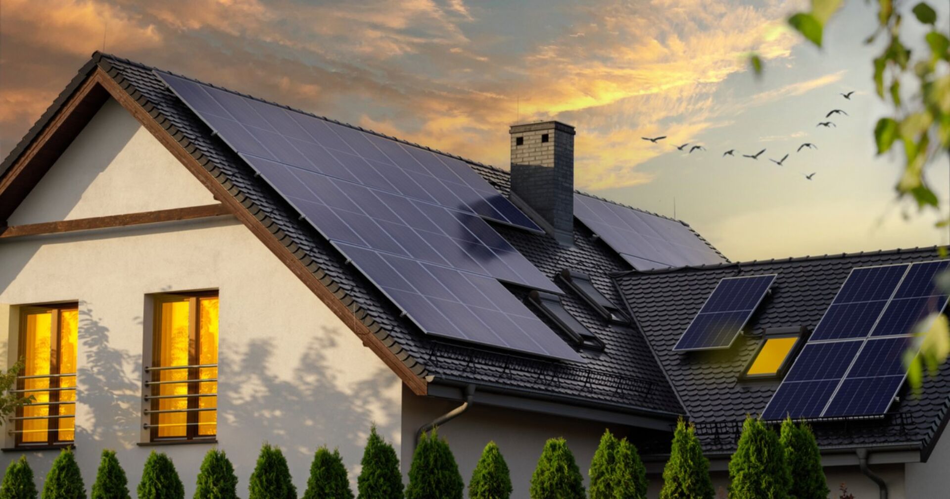 Es ist ein Haus zu sehen, dessen Dächer mit einigen Solarpanelen bedeckt ist und ein schöner blau sowie orange gefärbter Himmel.