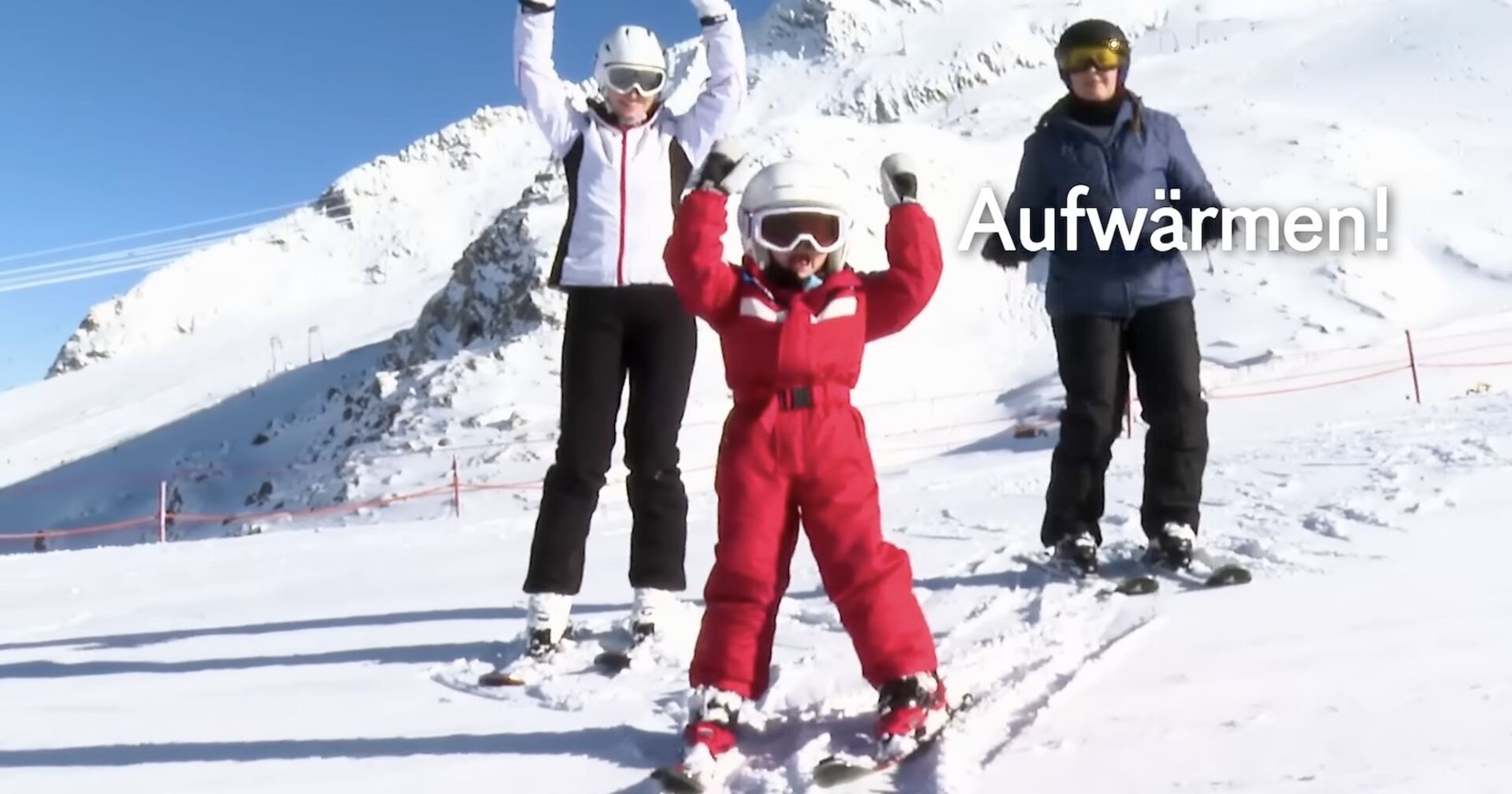 Charlotte zeigt zwei erwachsenen Skifahrerin Aufwärmübungen.