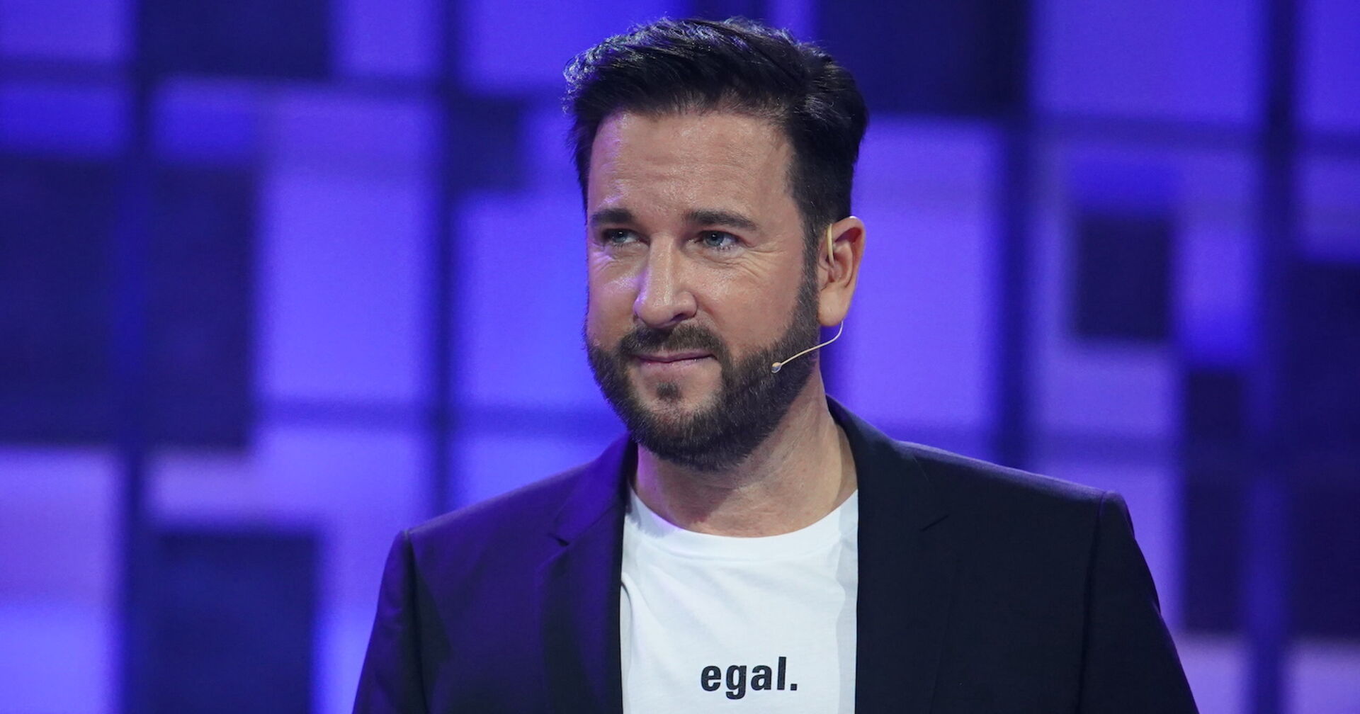 Michael Wendler in einem schwarzen Sakko mit einem weißen T-Shirt auf dem &quot;egal.&quot; steht.