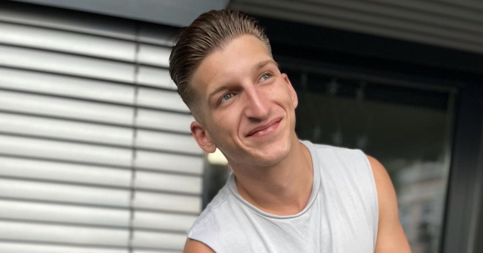 Satans Bratan grinst und trägt ein hellgraues T-Shirt.