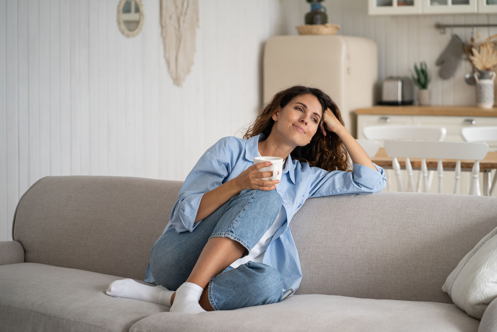 Frau sitzt auf Couch und trinkt Kaffee | Credit: iStock.com/Dima Berlin