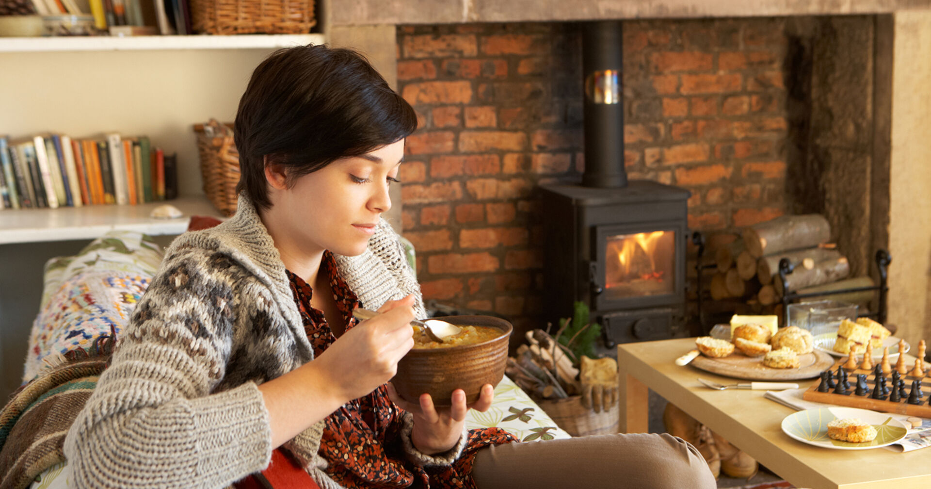 Frau isst Eintopf am Sofa | Credit: iStock.com/omgimages