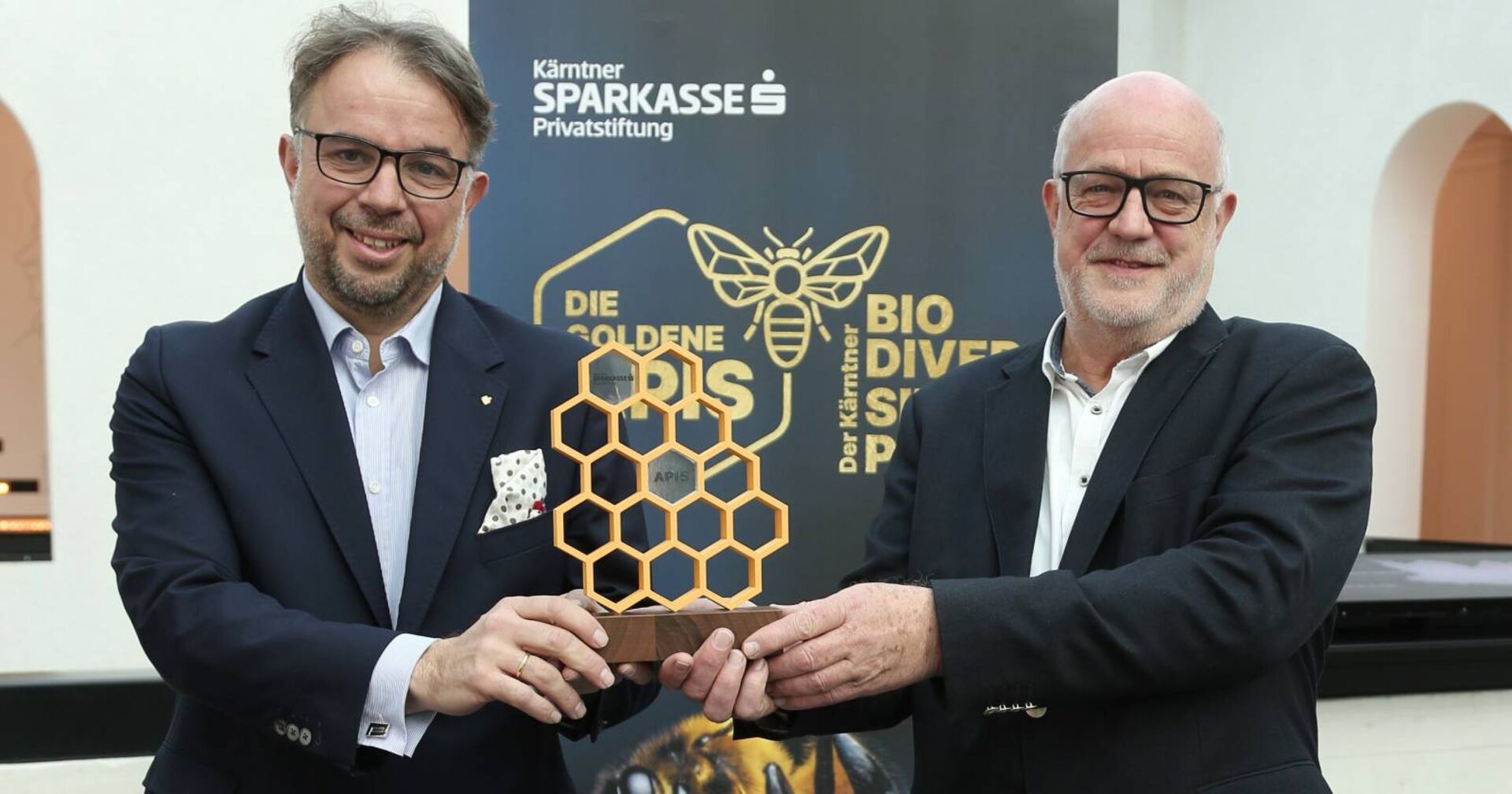 Die Vorstände der Privatstiftung Kärntner Sparkasse halten eine Trophäe, die einer Bienenwabe nachempfunden ist, in die Höhe