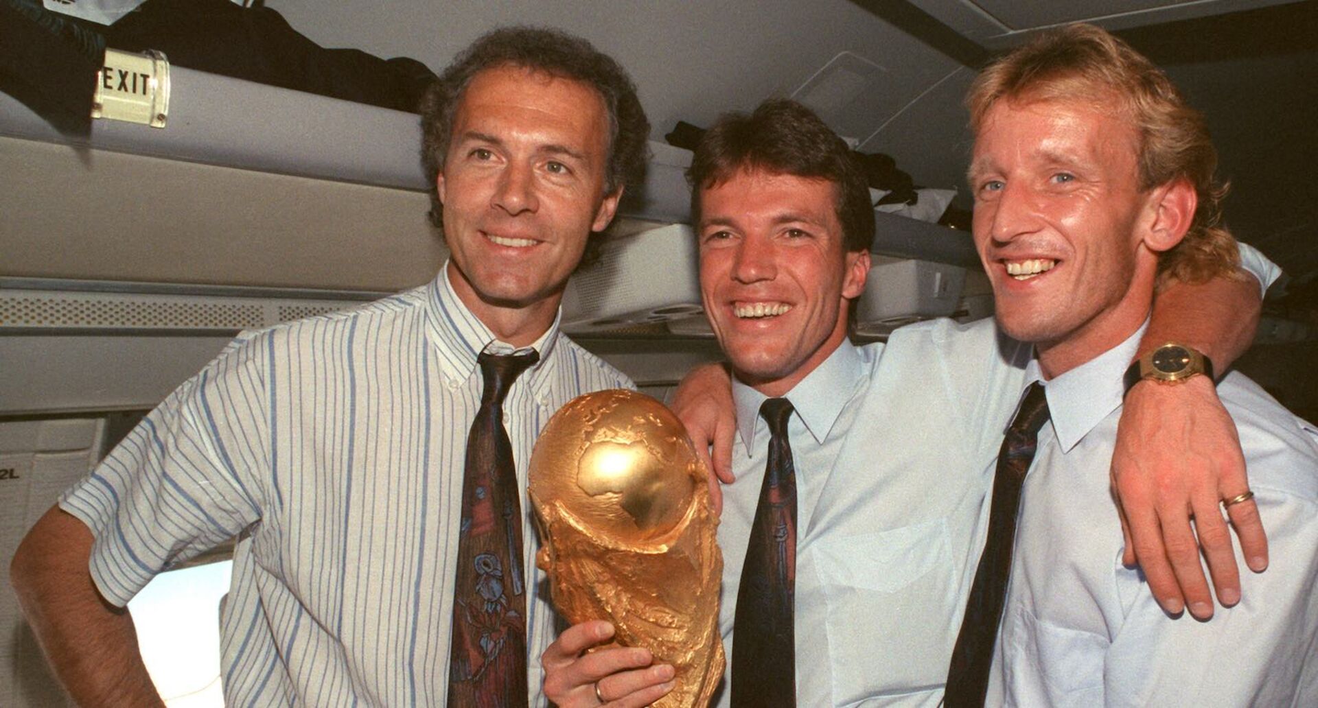 Andreas Brehme hält mit Lothar Matthäus und Franz Beckenbauer den WM-Pokal
