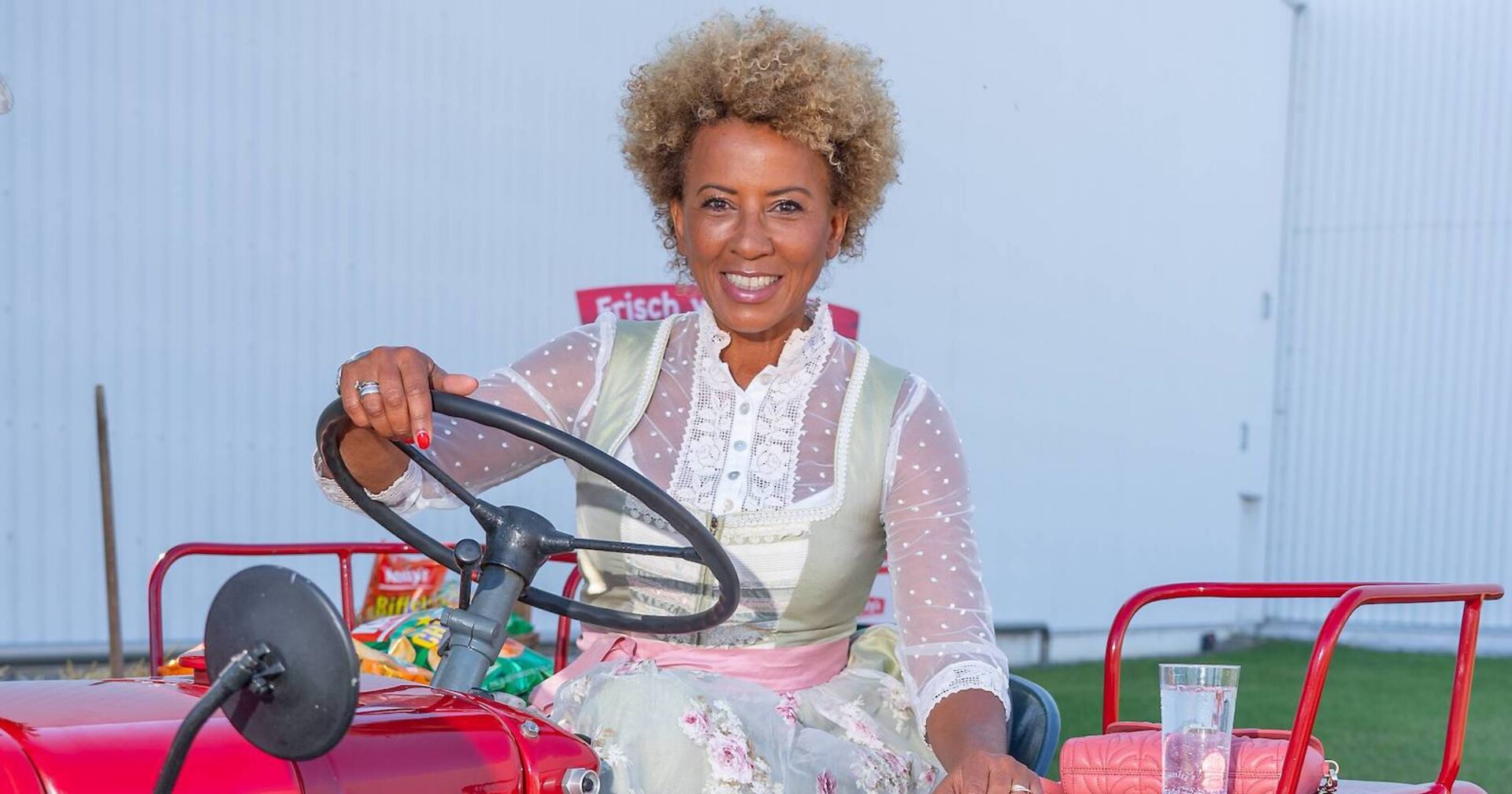 Arabella Kiesbauer im Dirndl auf einem Traktor.