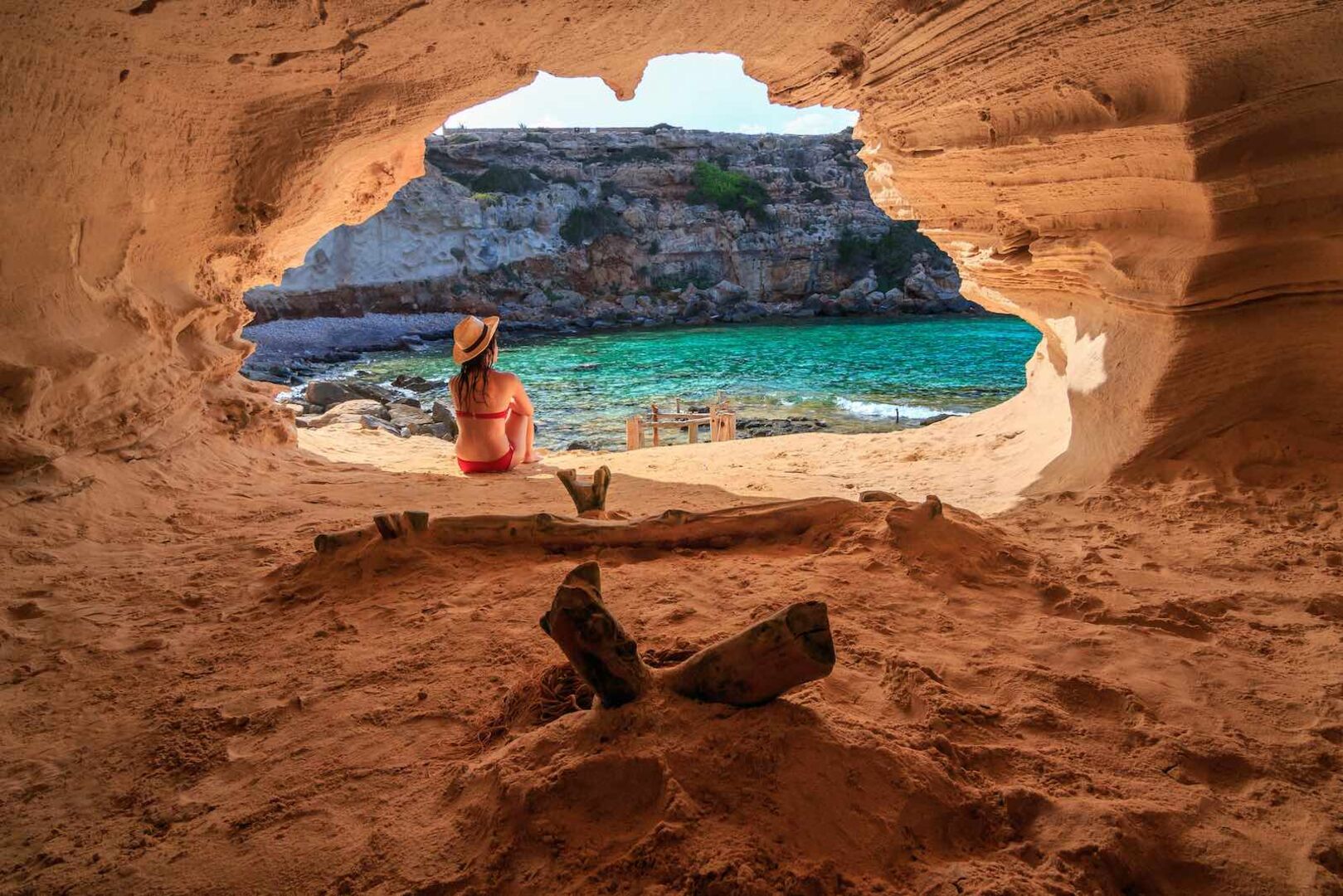 Eine Frau sitzt in einer Höhle vor dem Meer auf Formentera.