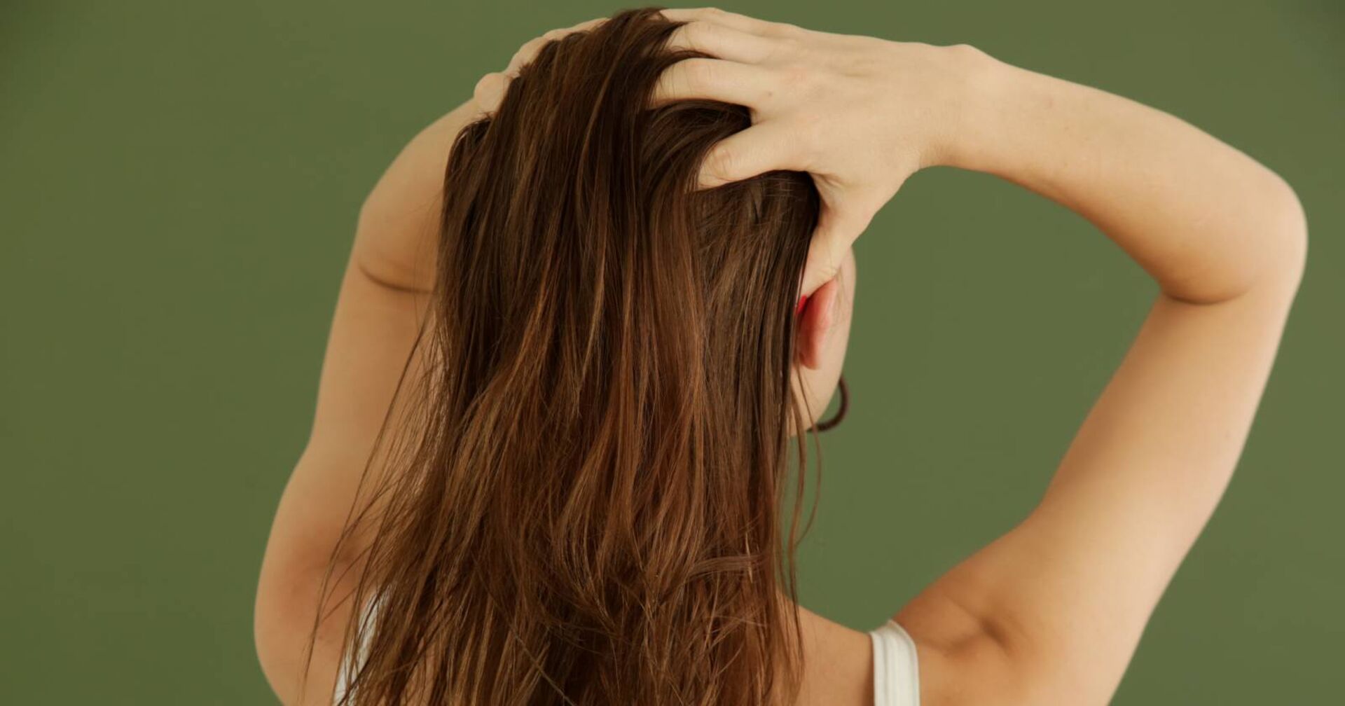 Frau verteilt Haaröl auf dem Ansatz ihrer dunkelbraunen Haare