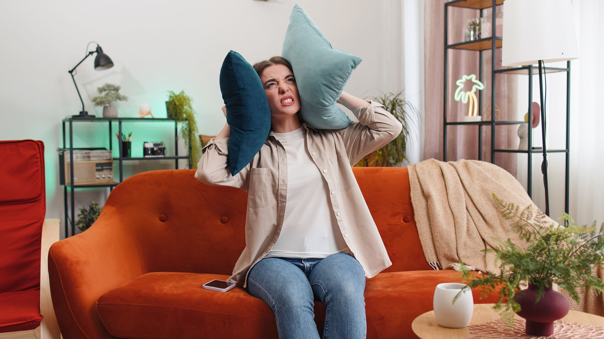 Frau hält sich mit Kissen die Ohren zu