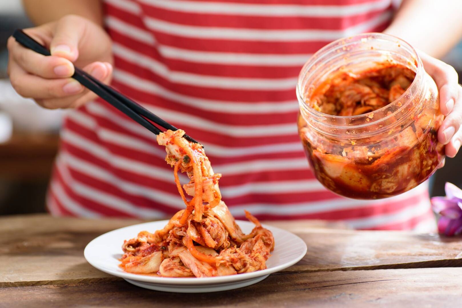 Koreanische Küche: Kimchi aus Kohl serviert in einem Glas neben weißen Tellern mit Essstäbchen. | Credit: iStock.com/Nungning20