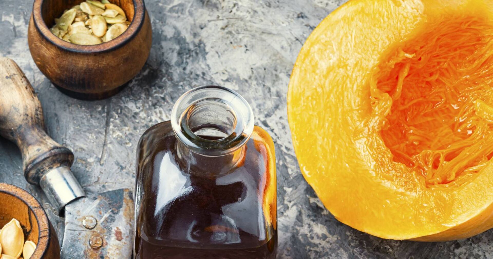 Symbolfoto eines aufgeschnittenen Kürbis, einer Glasflasche mit Kürbiskernöl und losen Kürbiskernen