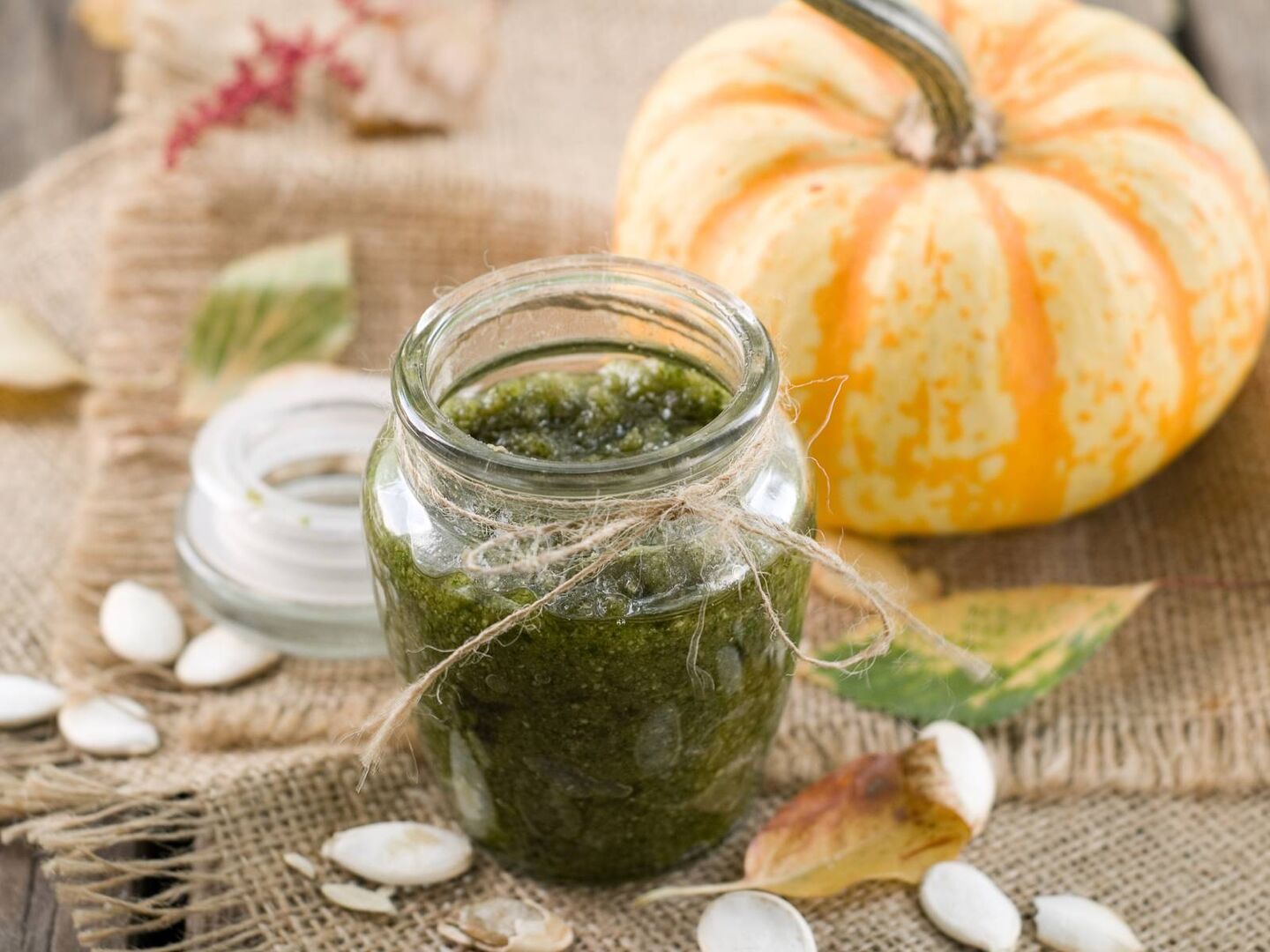 Kleine Flasche gefüllt mit grünem Pesto, im Hintergrund befindet sich ein ganzer Kürbis