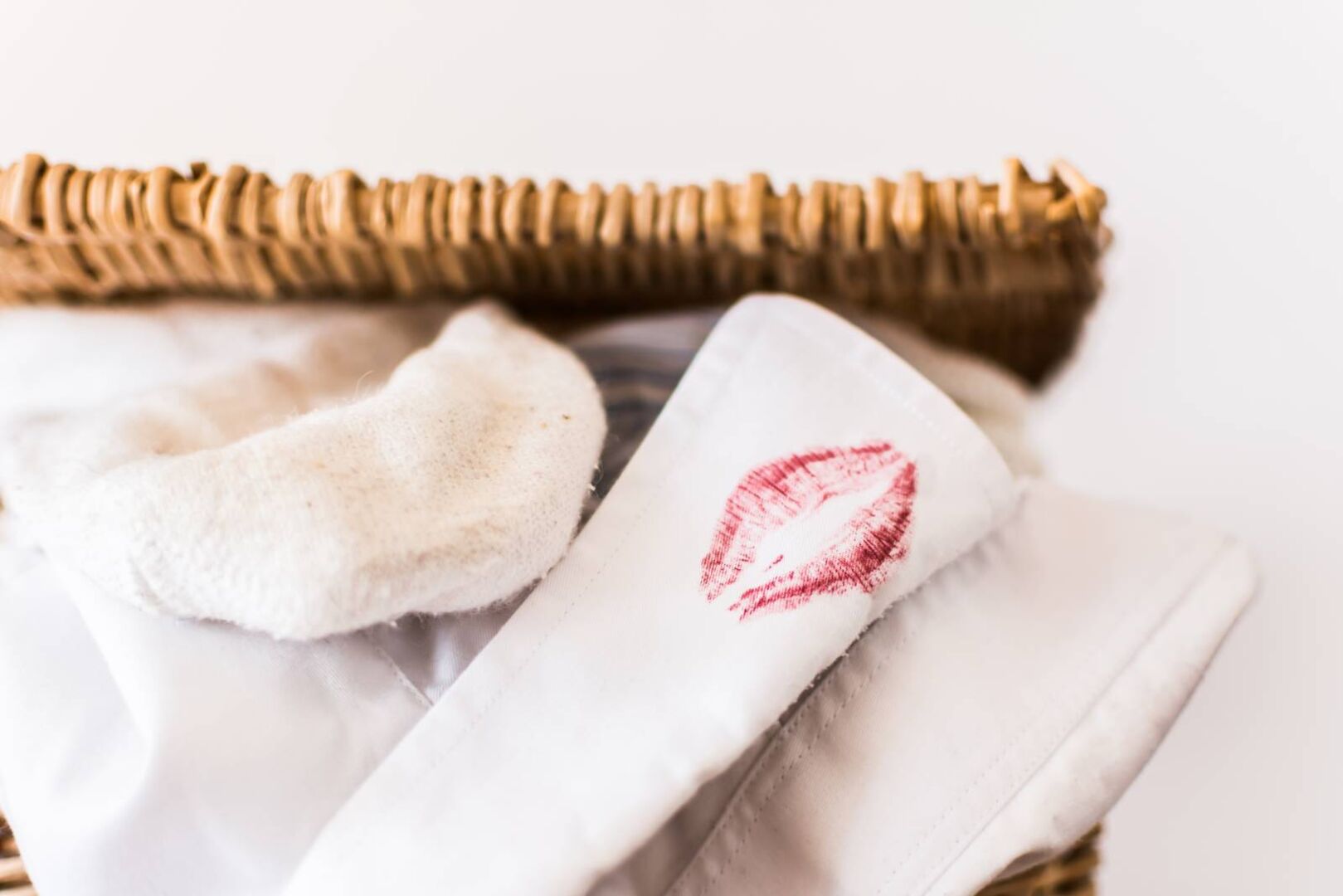 Roter Make-up-Kussmund-Fleck auf einem weißen Hemd in einem Wäschekorb