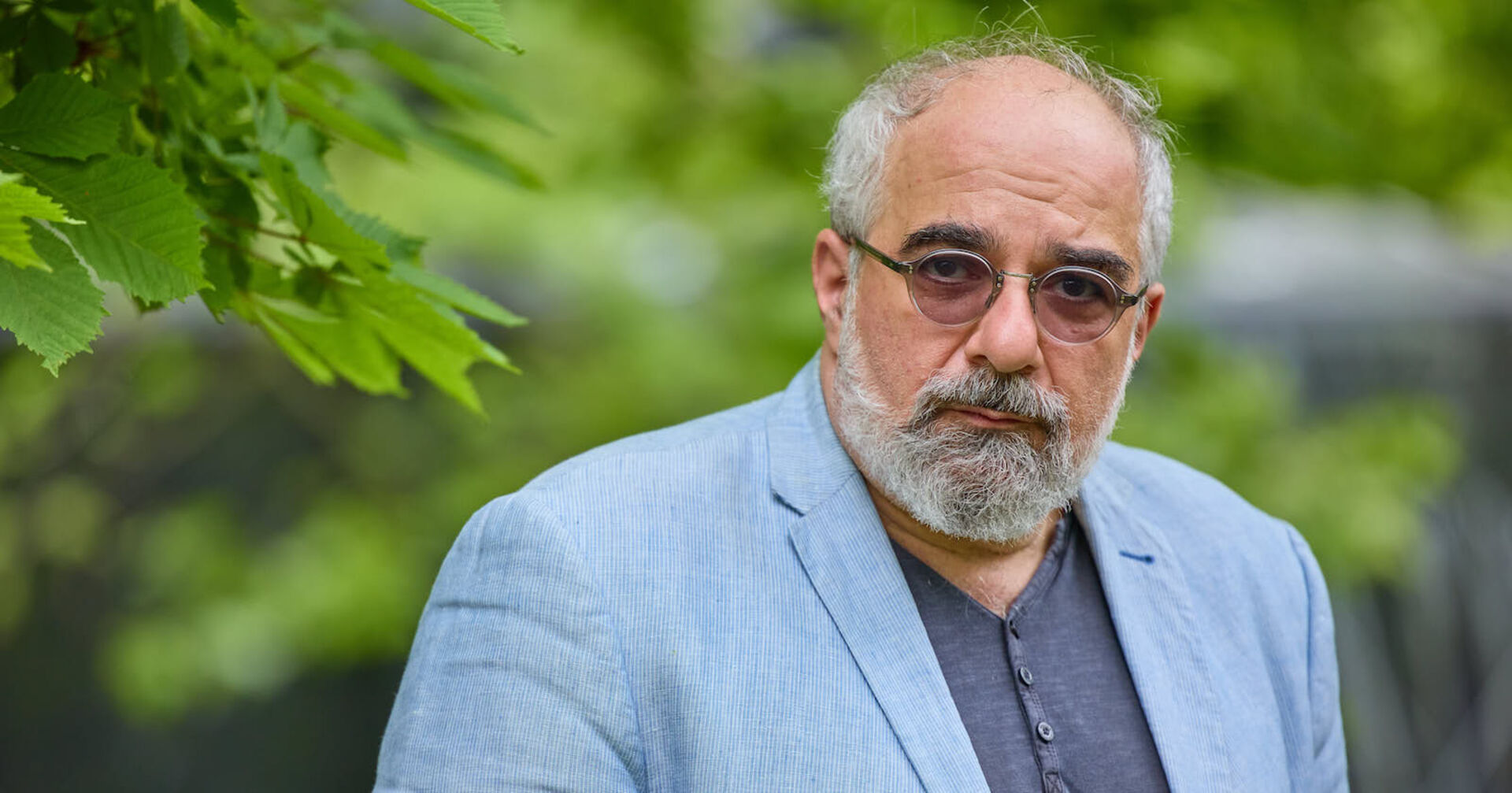 Michael Niavarani mit einem hellblauen Anzug und einer Sonnenbrille.