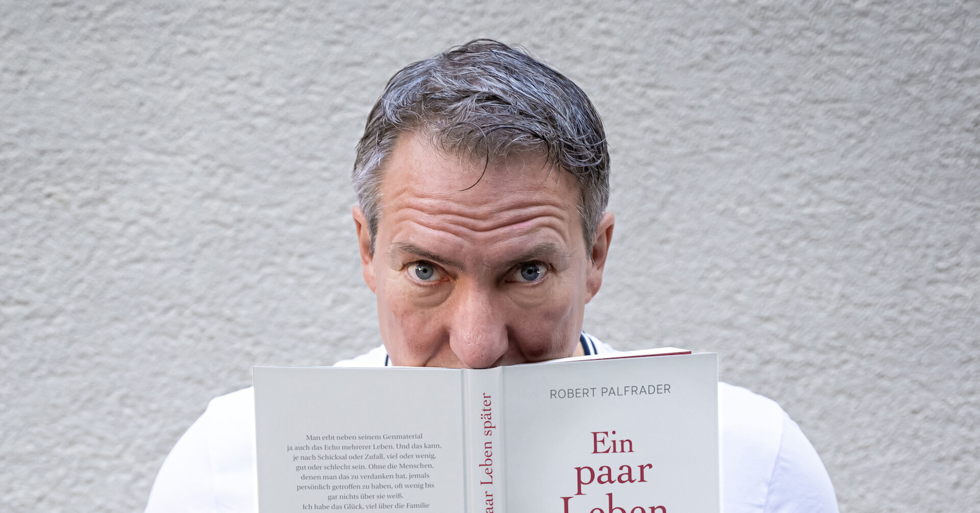 Robert Palfrader hält sein Buch &quot;Ein paar Leben später&quot; und schaut über den Rand hinweg.