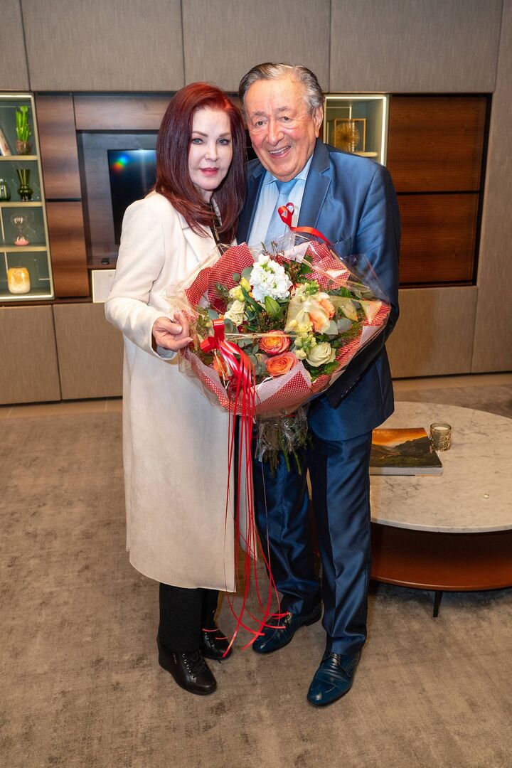 Priscilla Presley mit Richard Lugner. Beide halten einen Blumenstrauss.
