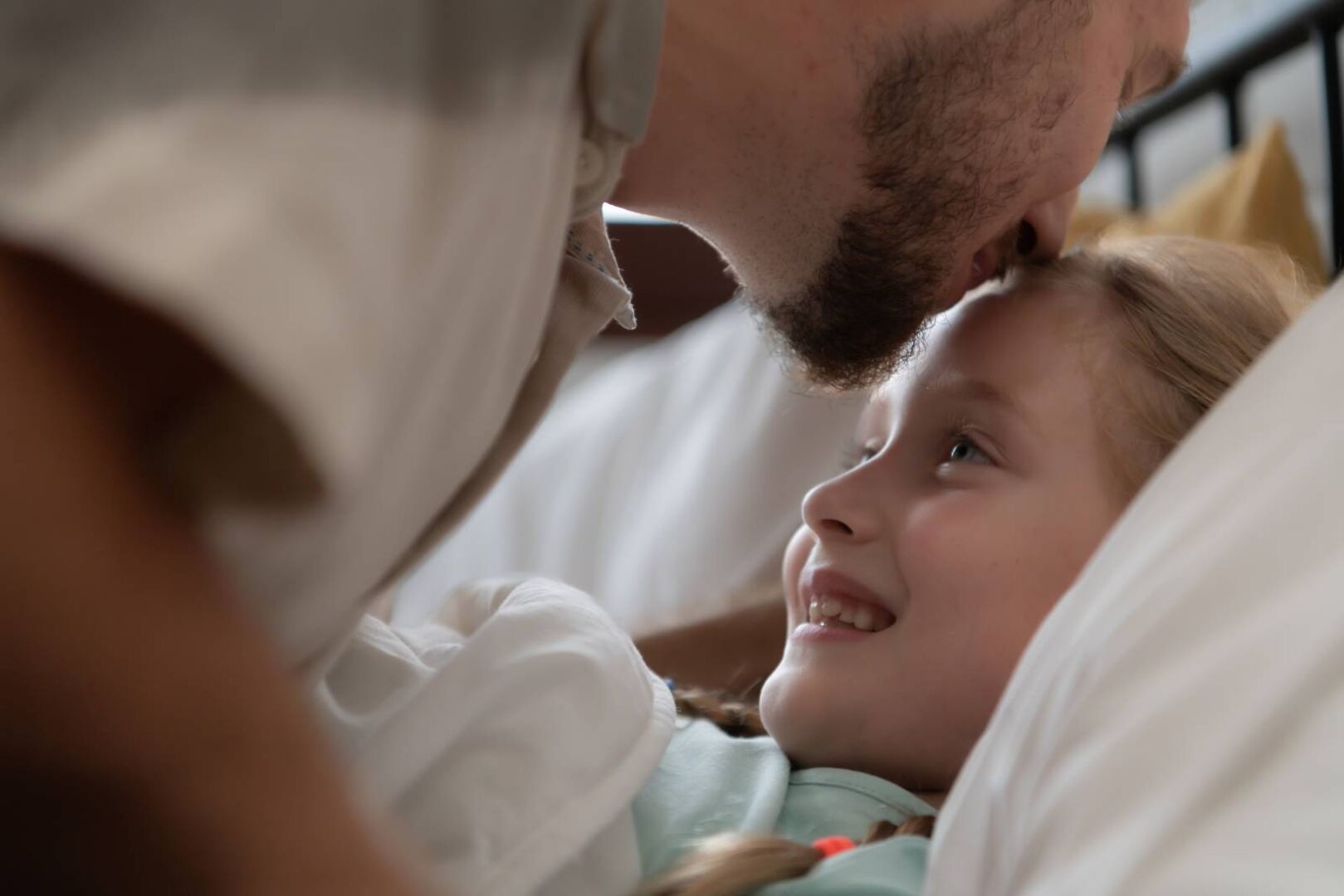 Der Vater zeigt seine Zuneigung, indem er das Kind beim Zubettbringen auf die Stirn küsst.