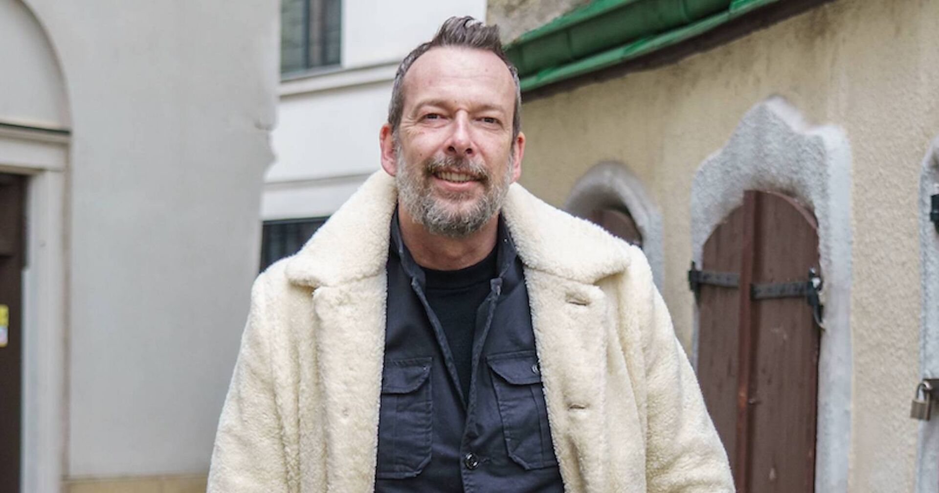 Robert Kratky mit einem weißen Teddy-Mantel in der Innenstadt in Wien-