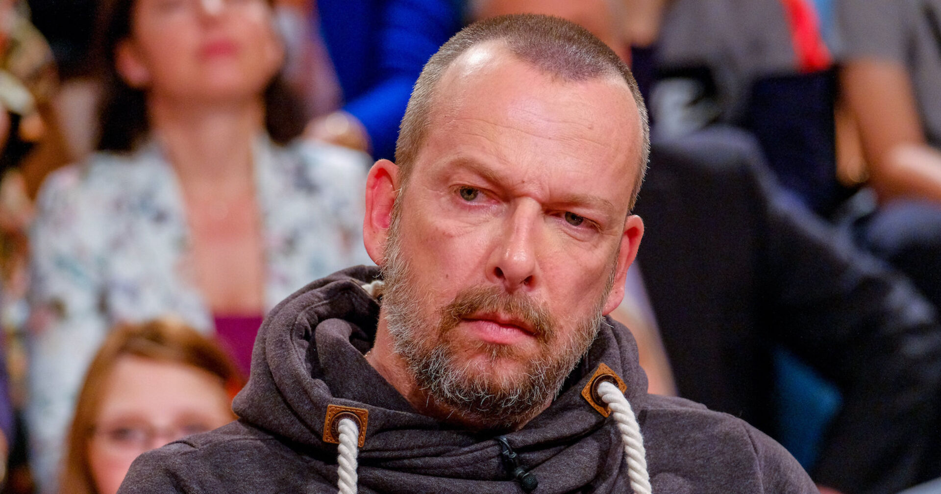 Robert Kratky mit einer Stoppelglatze und einem Pullover vor einer Audience.