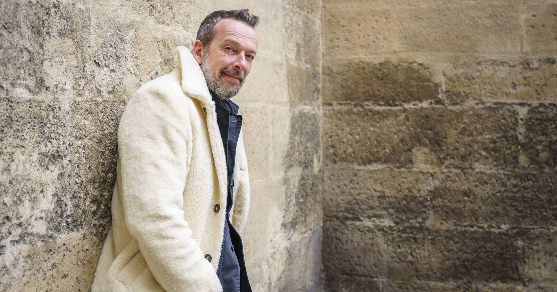 Robert Kratky in einem weißen Mantel an einer Mauer.