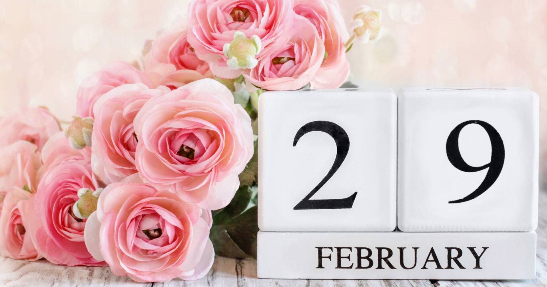 Übereinander gestapelte weiße Holzklötze, die zusammengesetzt den &quot;29. Februar&quot; ergeben, verziert mit rosa Rosen.