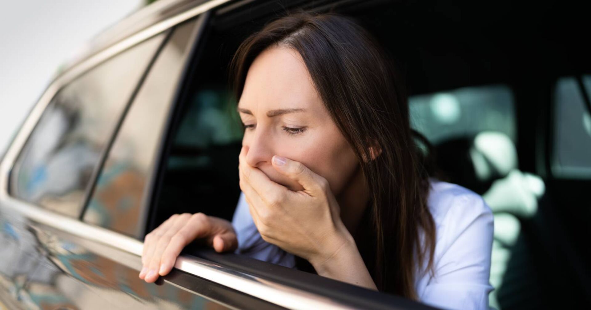 Junge Frau lehnt sich wegen Übelkeit aus dem Autofenster
